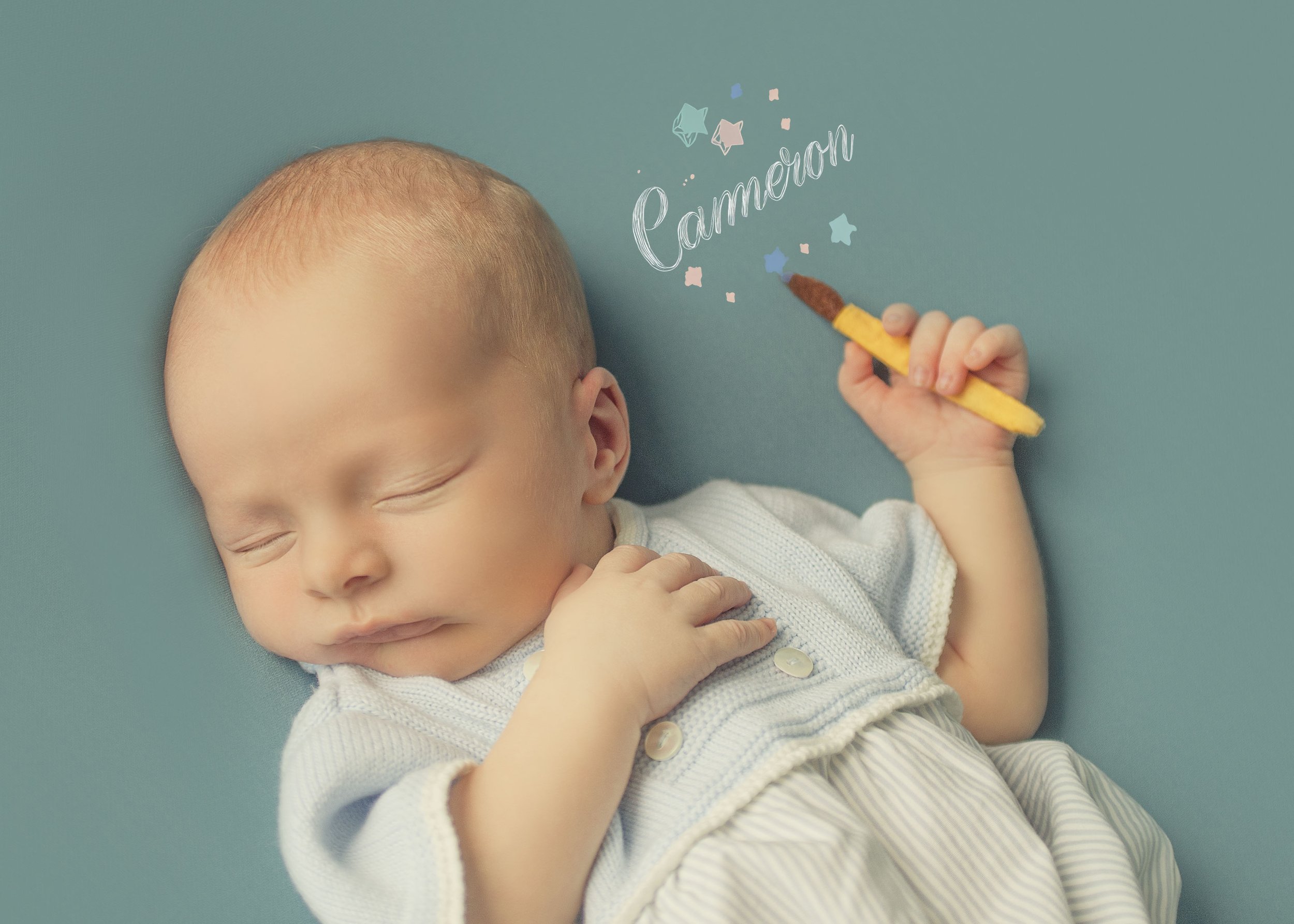 Recién nacido durmiendo, sosteniendo un lápiz de colores y dibujando la palabra 'Camerón' en la imagen