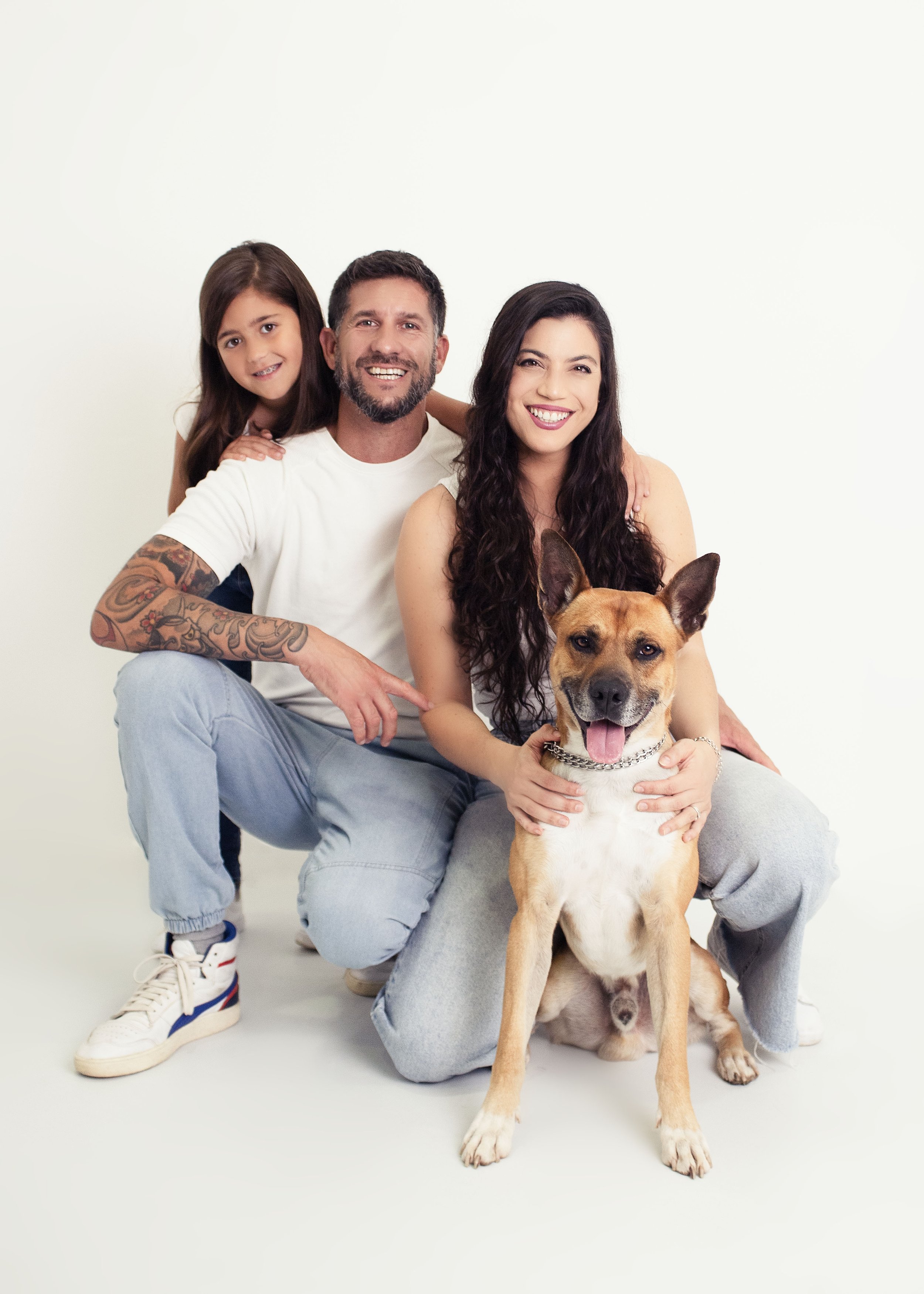 Familia sonriente con un perro en un fondo blanco.