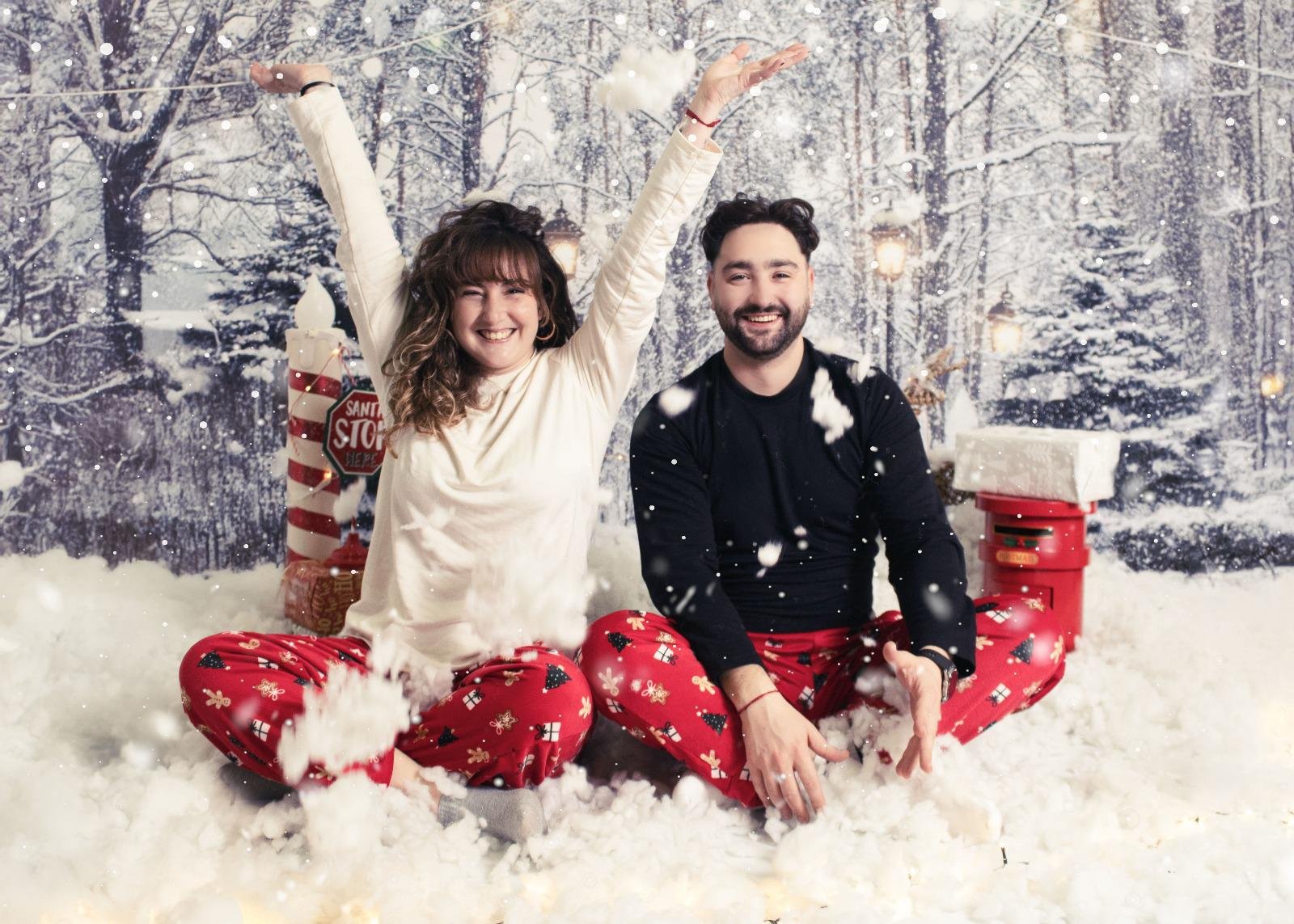 Los fotógrafos  sonriendo y jugando en la nieve en un escenario navideño con árboles cubiertos de nieve y decoraciones festivas.