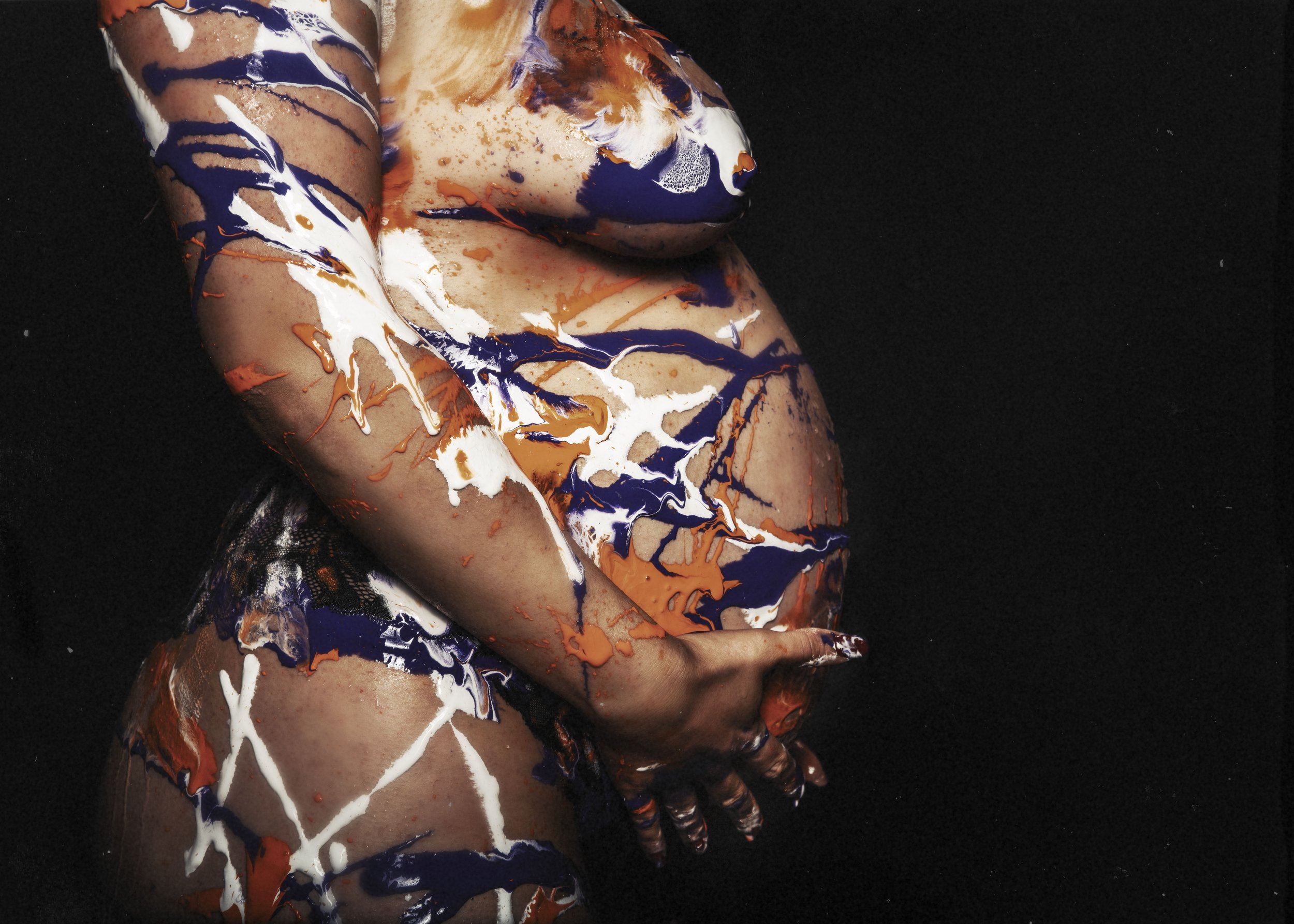 Cuerpo embarazada  cubierto con pintura de colores blanco, azul y naranja en fondo negro.