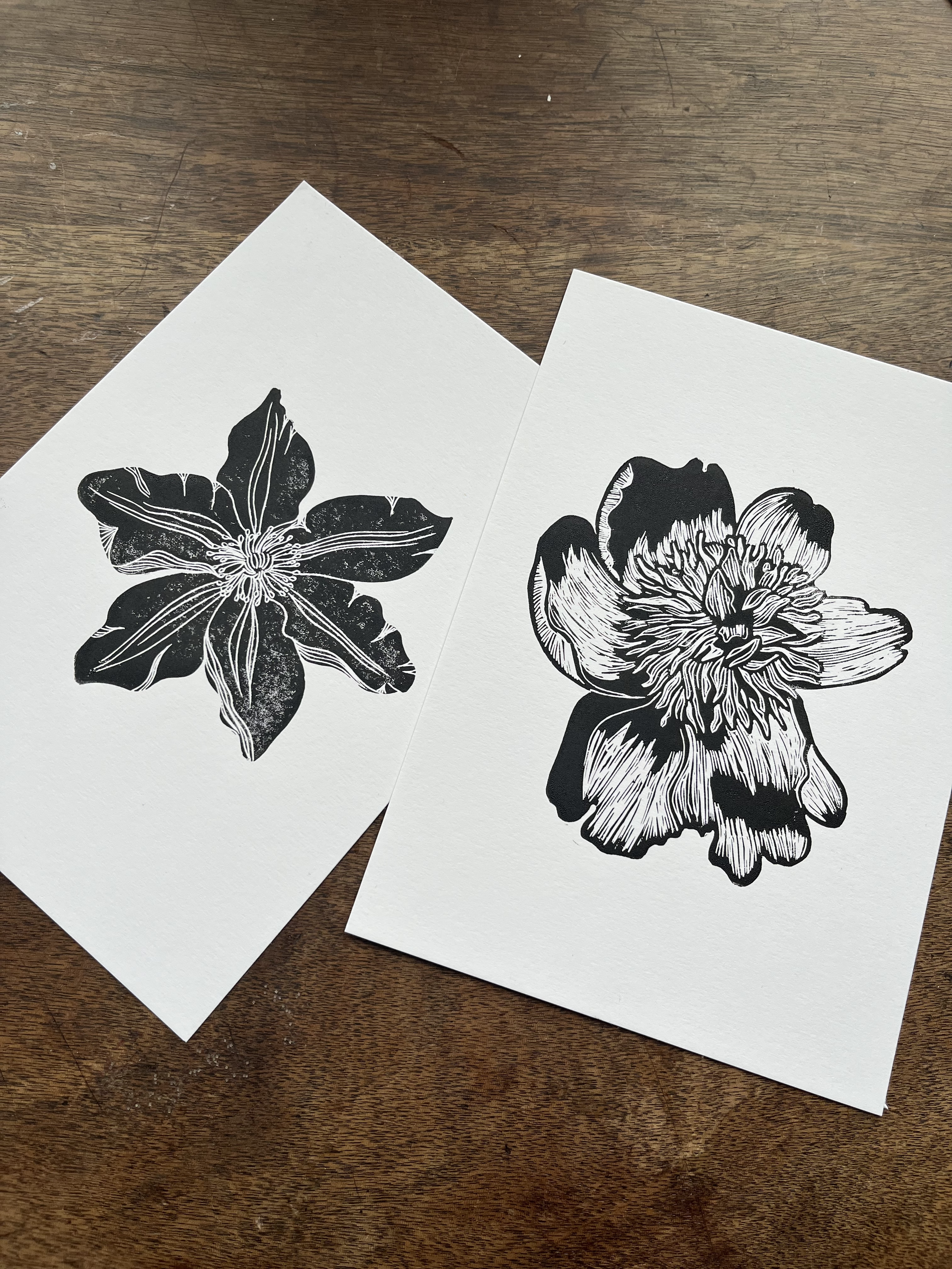 Two black and white floral prints on white paper, placed on a wooden surface.