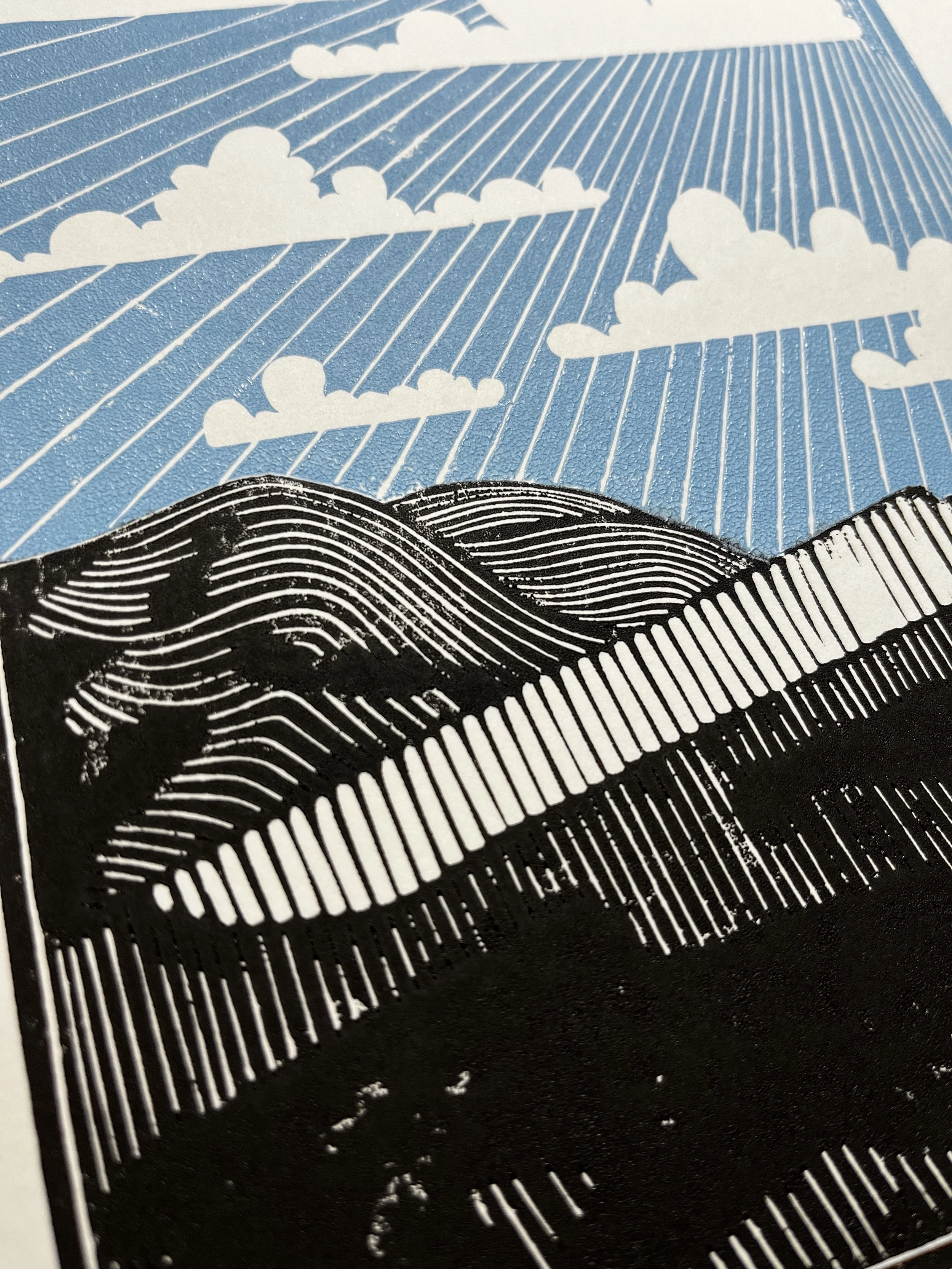 Close-up of a colorful illustration featuring clouds, rain, and rolling hills with stylized lines, using black, white, and blue colors.