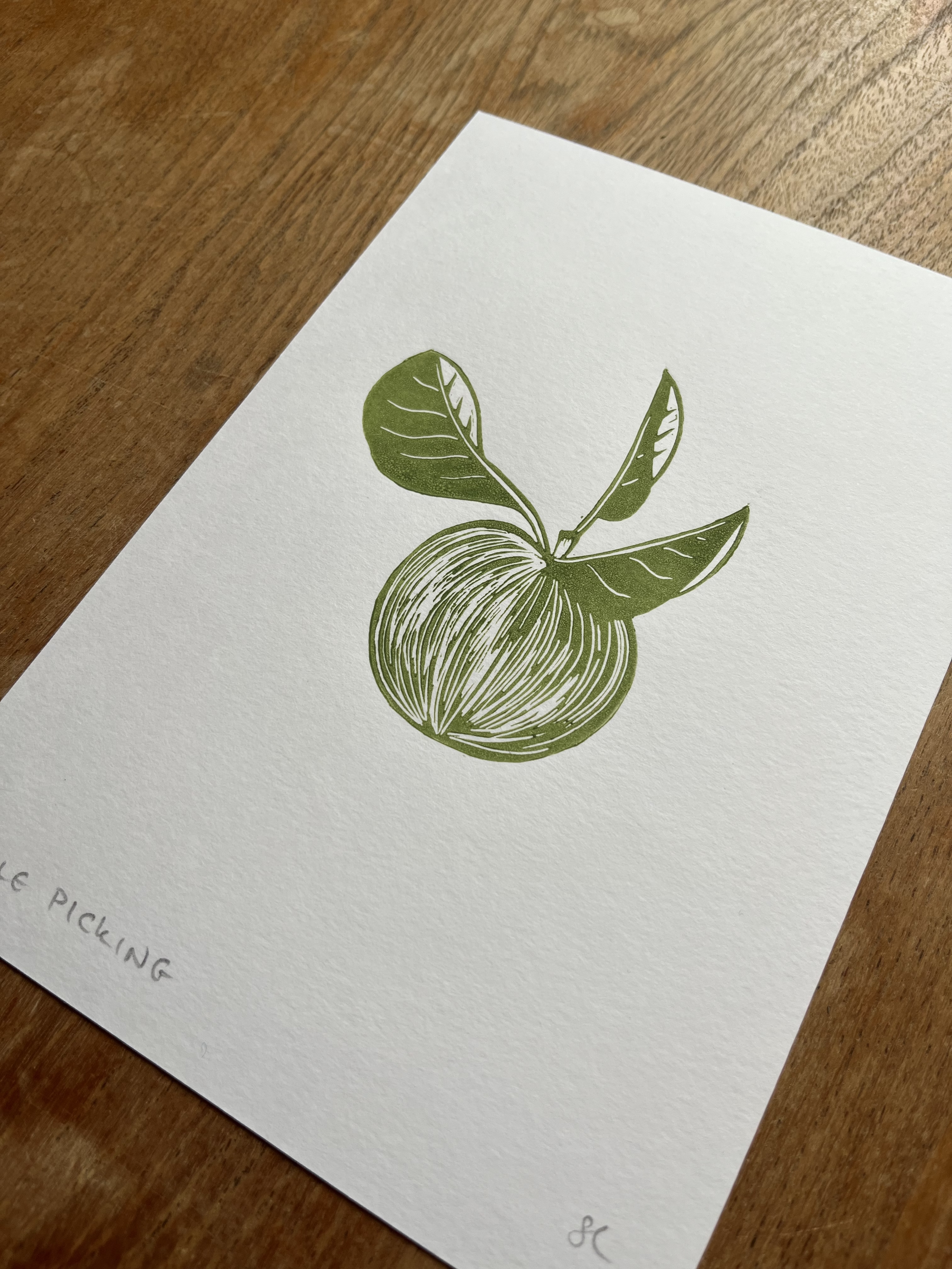 A white sheet of paper with a green illustration of an apple with leaves, partially on a wooden surface.