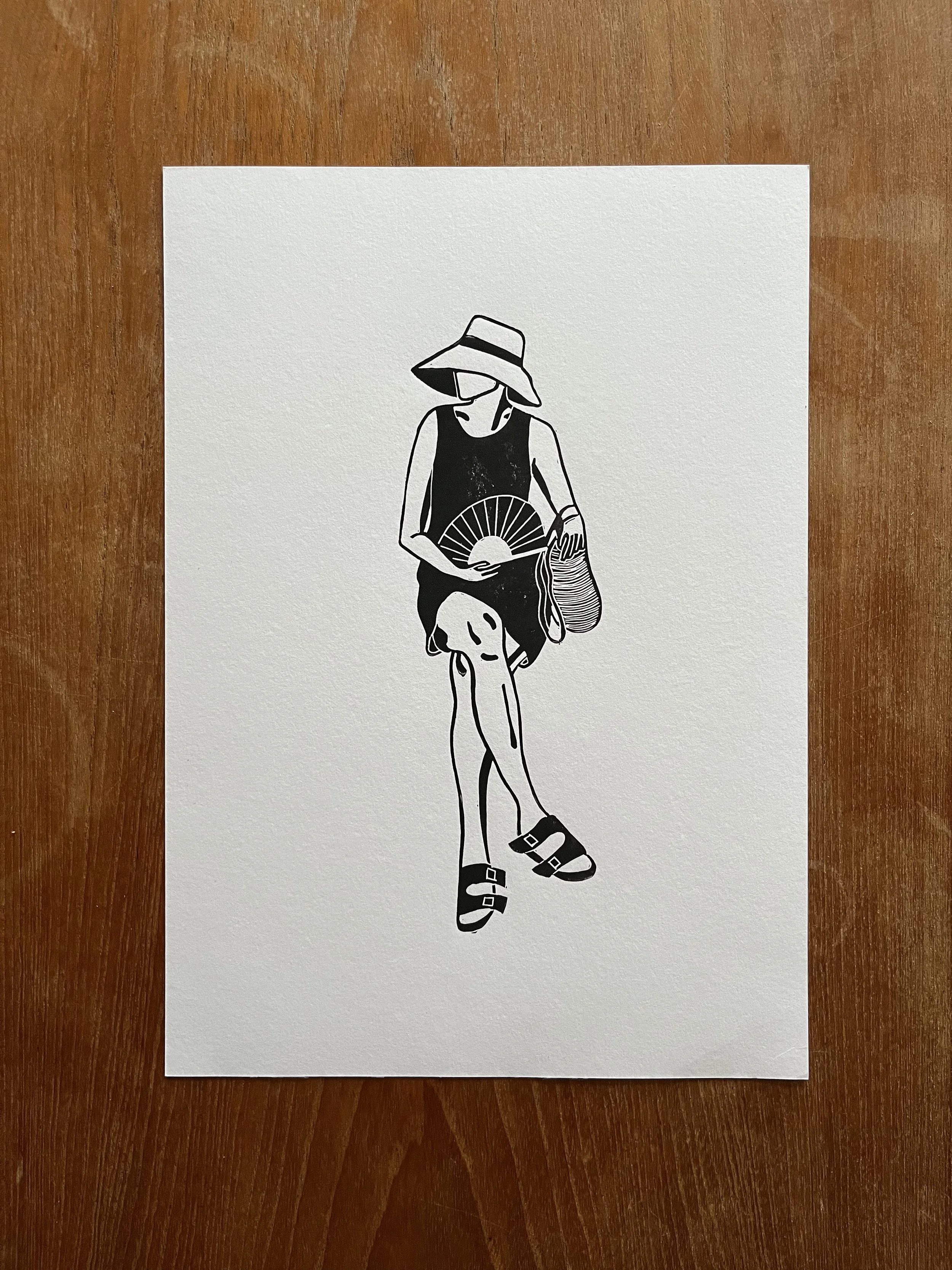 Black and white illustration of a woman sitting, wearing a large sun hat, sunglasses, a sleeveless dress, sandals, and holding a fan and a bag, on a wooden surface.