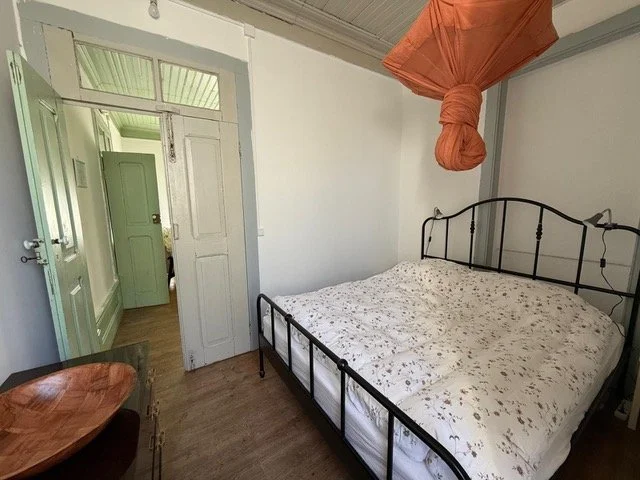 bedroom of a rural holiday apartment in central Portugal with double bed, doorway, wooden floor, cabinet, and hanging mosquito net