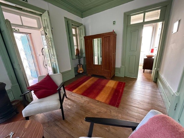 living room interior of a countryside holiday apartment in central Portugal with traditional wooden floor, armchair, doorway to another room, and a guitar below the window