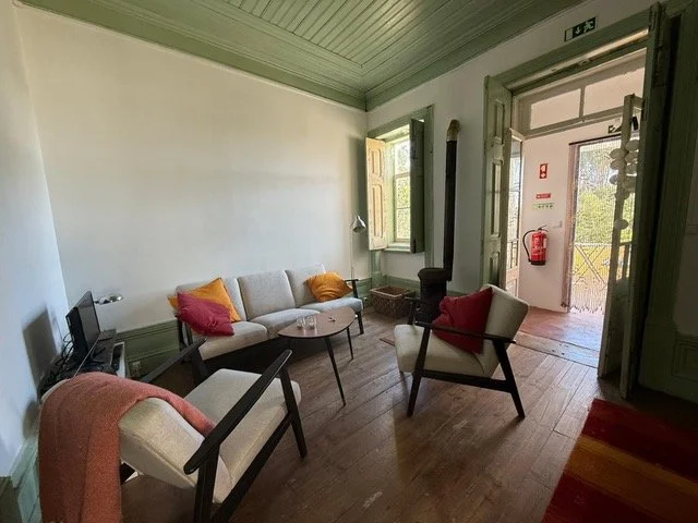 living room of a rural holiday apartment in central Portugal with sofa, armchairs, wooden floor, and open door to a terrace