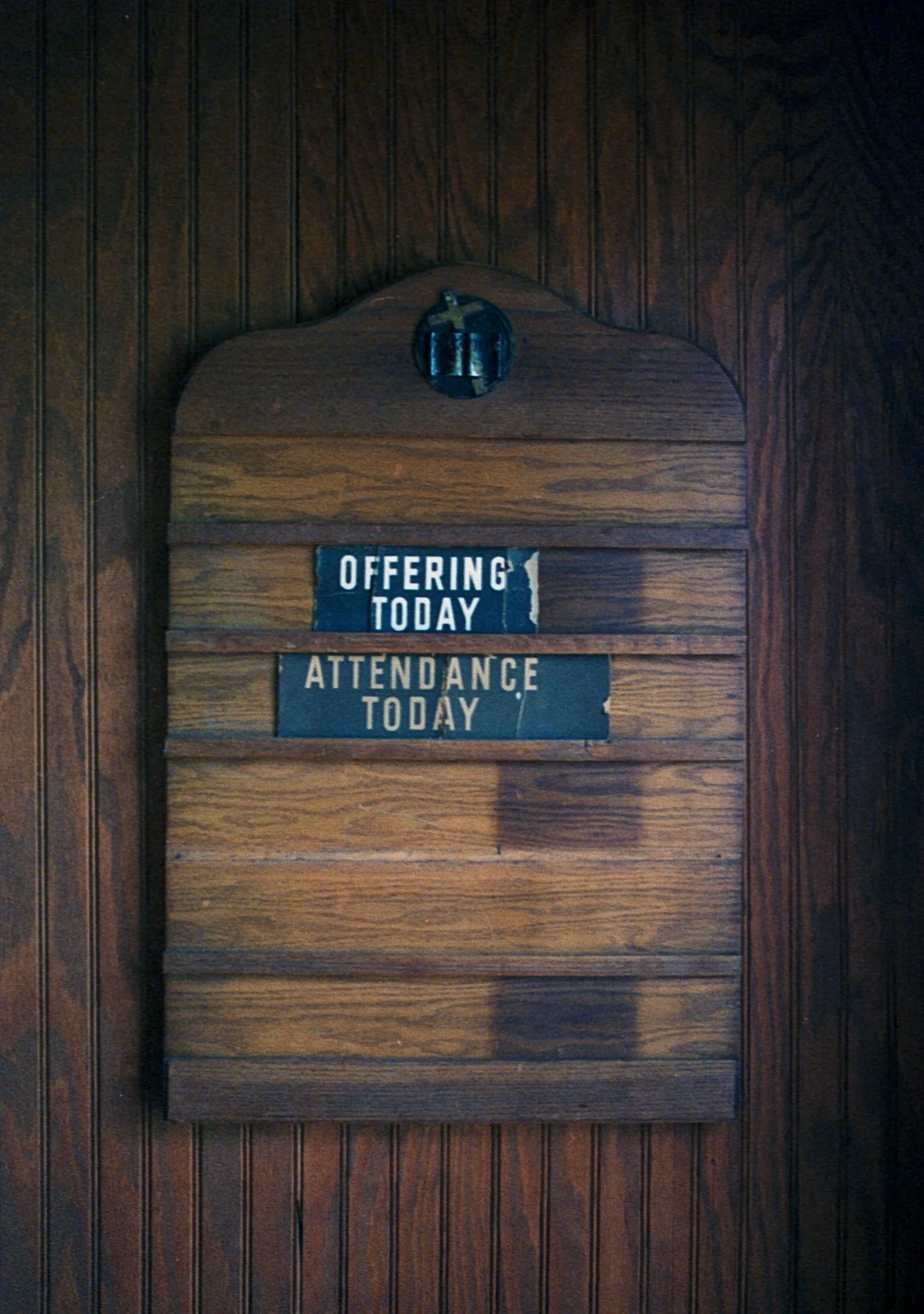 Wooden wall with a small sign that reads 'Offering Today: Attendance Today' and a circular electrical outlet above the sign.