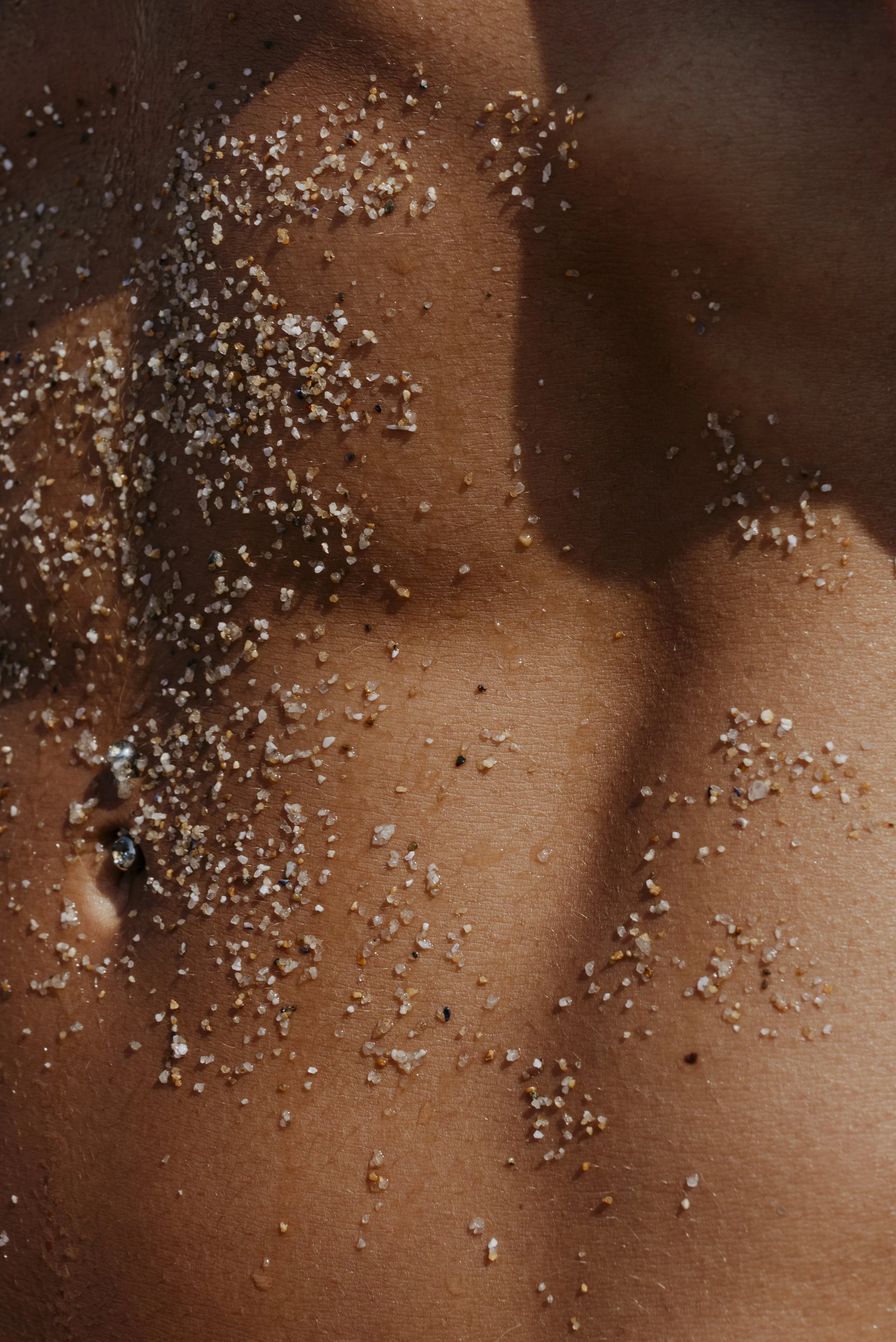Close-up of a person's skin with small grains of salt and a pierced earlobe with a gemstone piercing.