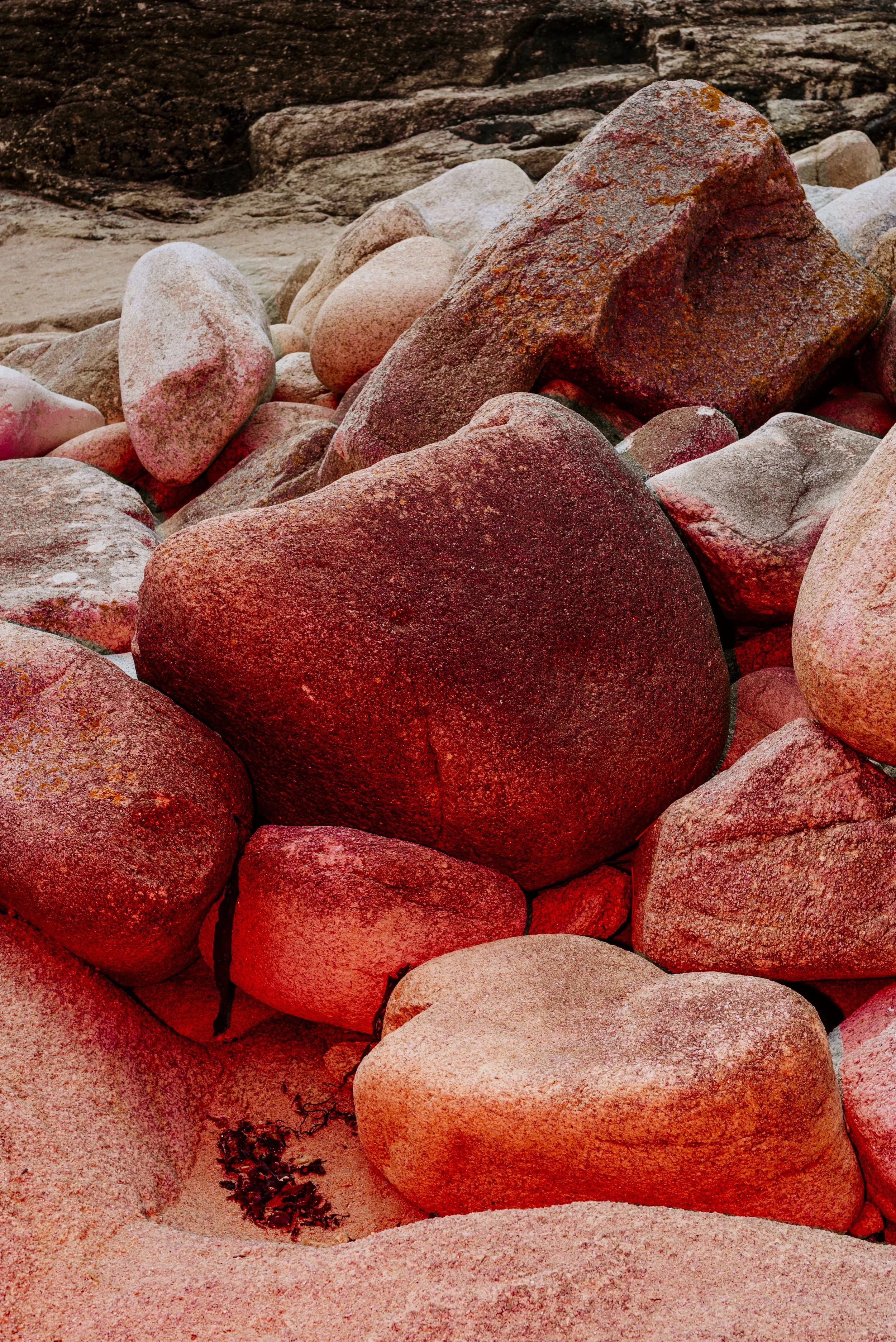 Large reddish rocks on a beach with some sand and seaweed at the bottom.