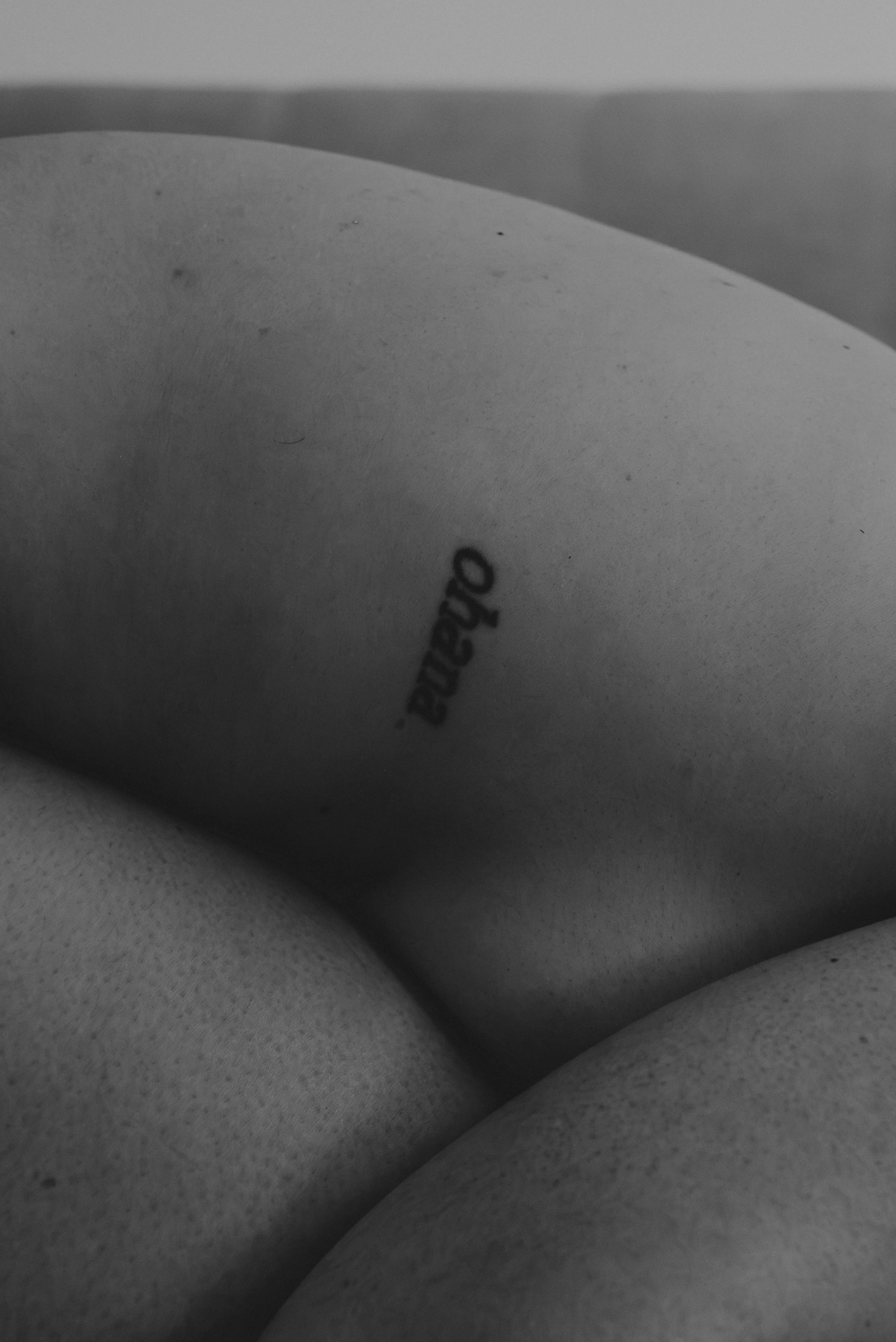 Close-up black and white photo of a person's bare legs and part of their torso, with the word 'andrea' visible on the skin.