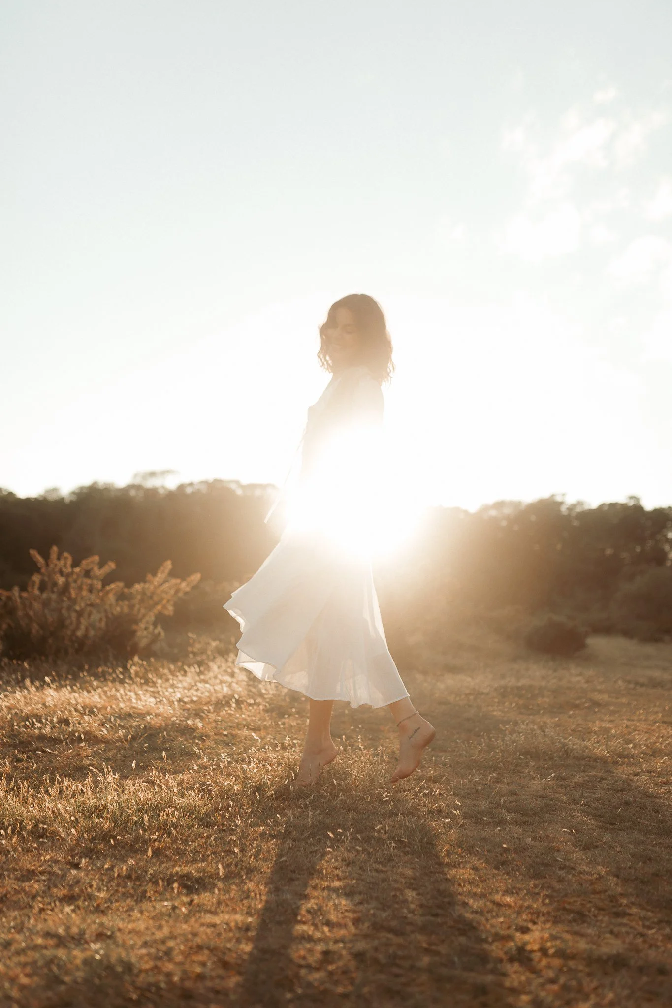 Double exposure photo of a person with outstretched arms holding flowers, overlaid with bright yellow flowers and sunlight in a field during sunset.