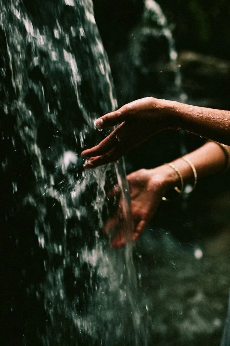 Close-up of a person's hand touching flowing water in a natural outdoor setting.