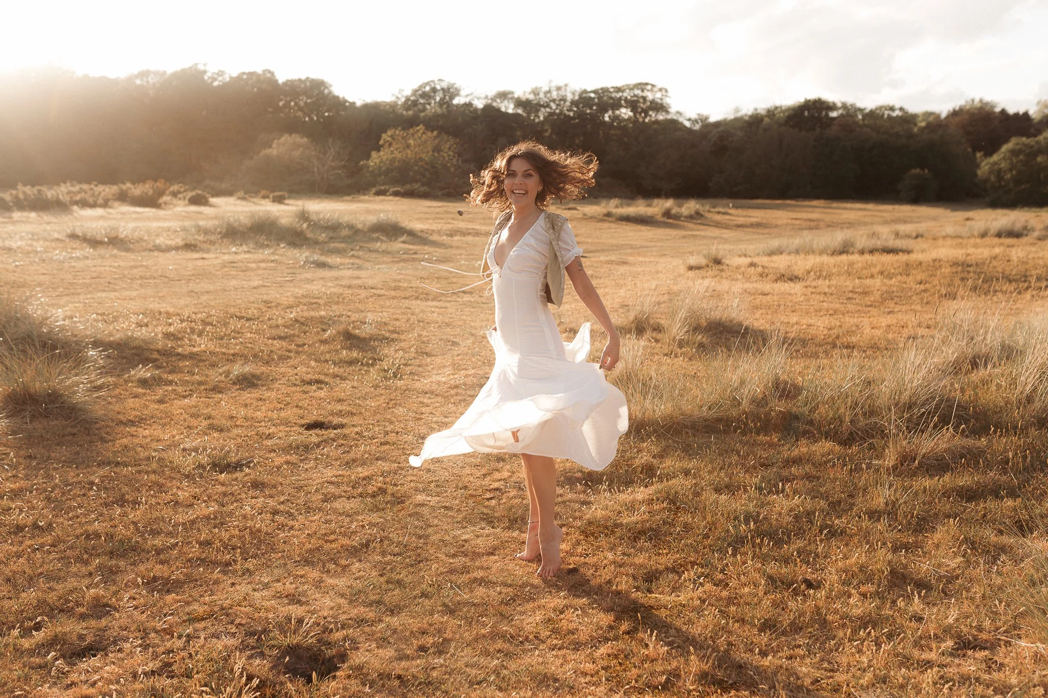 Close-up of a person's hand holding a flower in a field during sunset, with soft sunlight illuminating the scene.