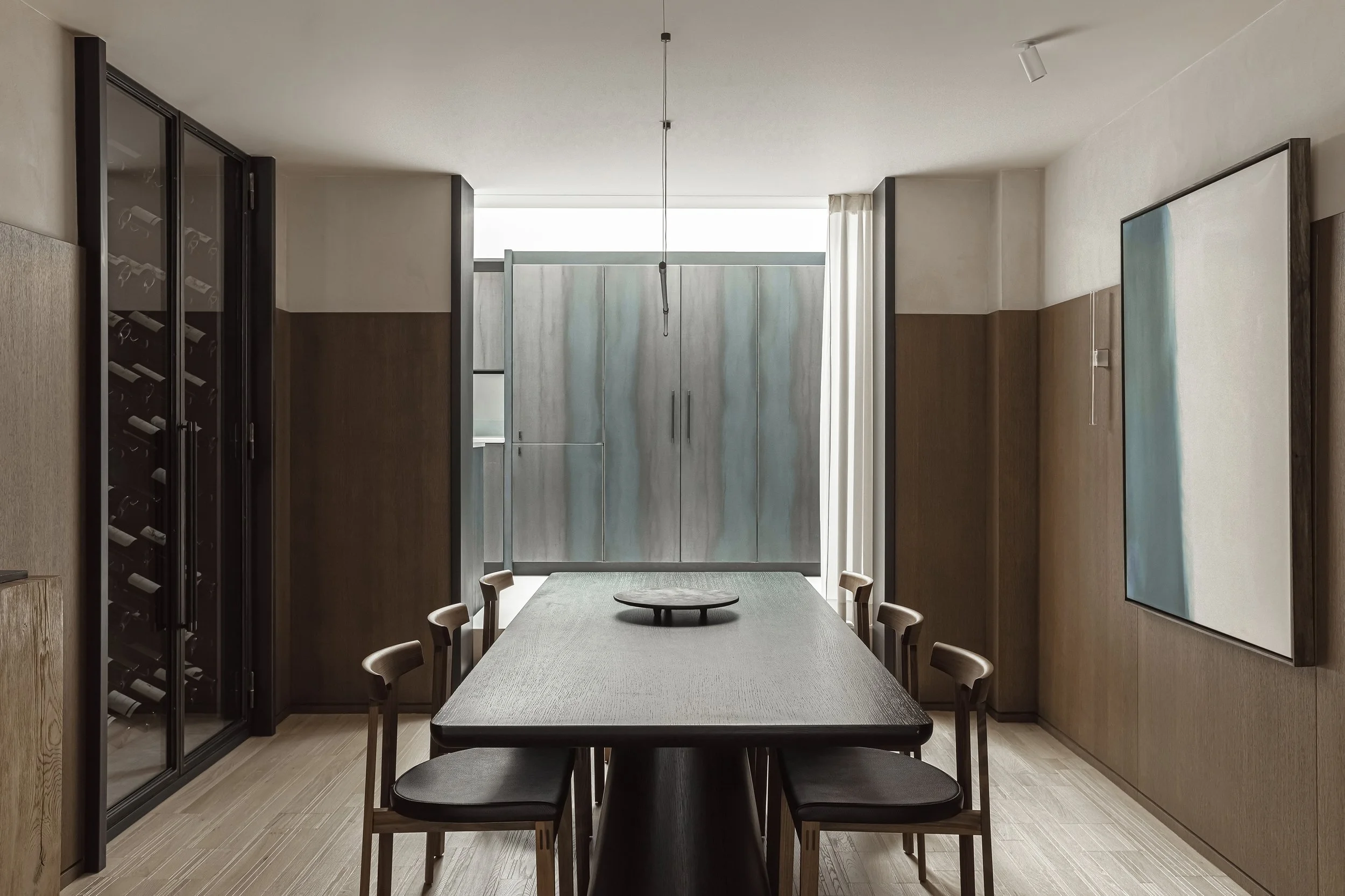 Contemporary dining room within a luxury Chelsea townhouse renovation in London, featuring dark timber panelling and integrated kitchen design.
