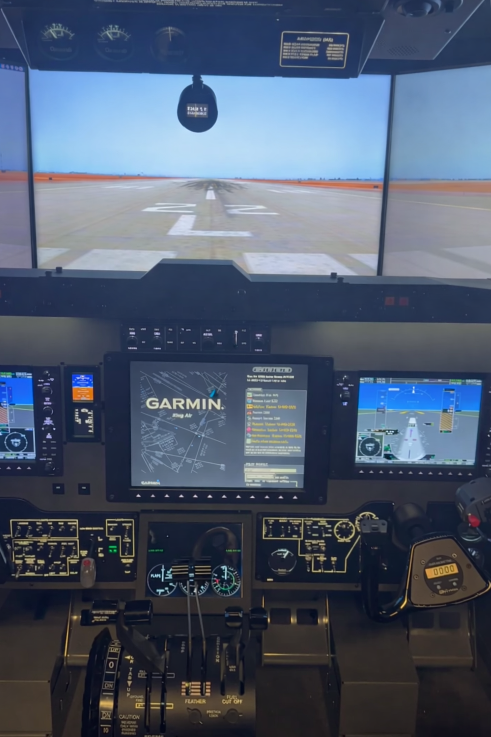 The image shows the cockpit of an aircraft with various control panels and digital screens. The view outside the cockpit window reveals the runway, ready for takeoff or landing.