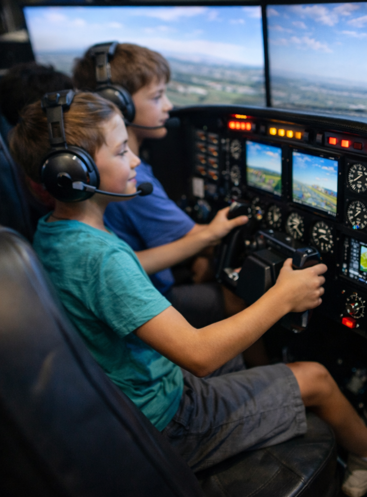 Two children sitting in the cockpit of a small aircraft, wearing headsets, with a view of the sky and landscape outside the windows, operating the flight controls.