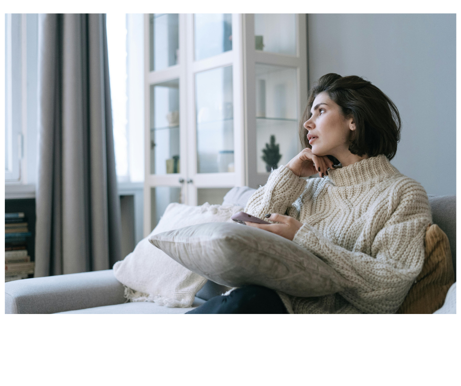 Woman sitting quietly on a couch in thoughtful reflection, representing the experience of anxiety, overwhelm, and the mental load many women carry.
