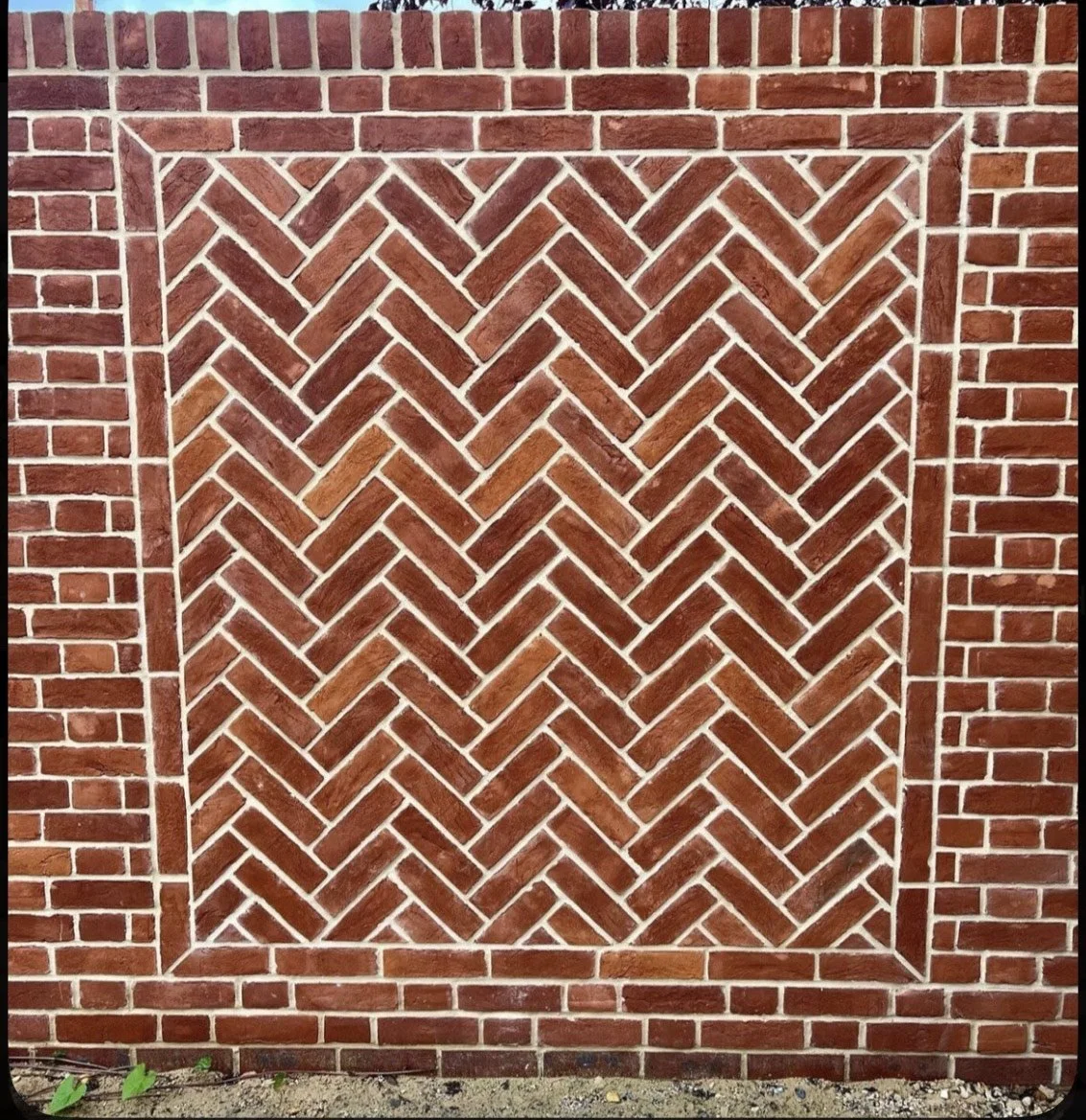 Red brick wall featuring a herringbone pattern framed by standard brickwork.