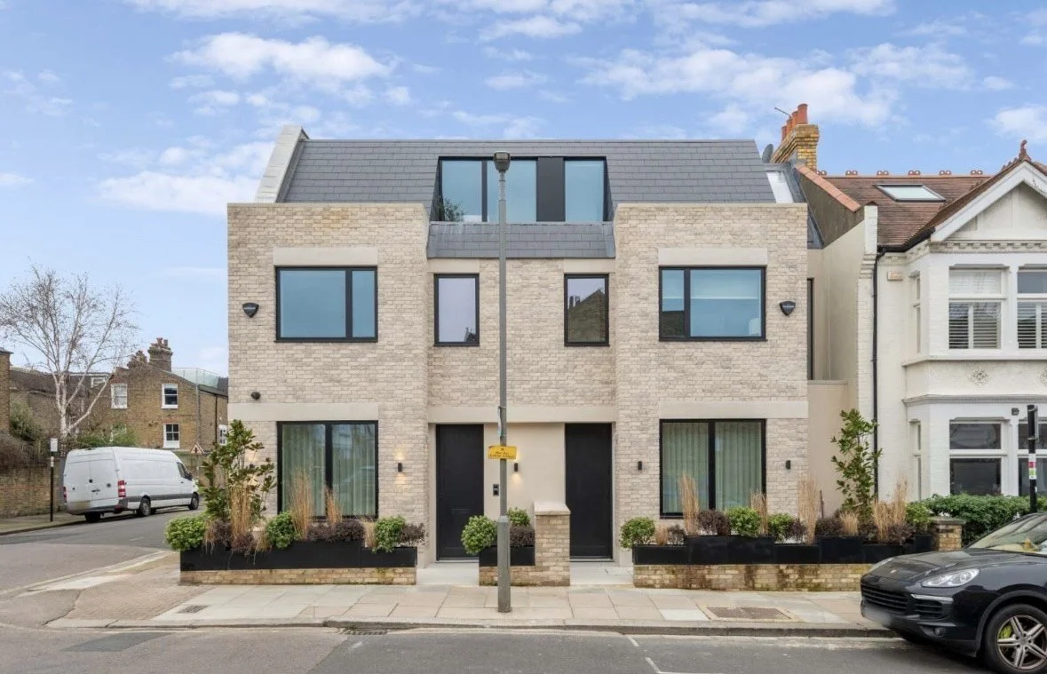 Modern multi-story residential building with brick exterior, large windows, and minimalist landscaping in the front yard, located on a city street.
