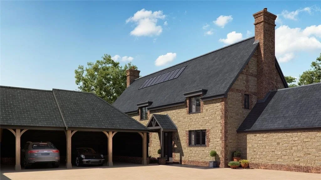 A large stone house with a gabled roof, chimney, and solar panels, situated in a green space with trees, and a covered parking area with three cars.