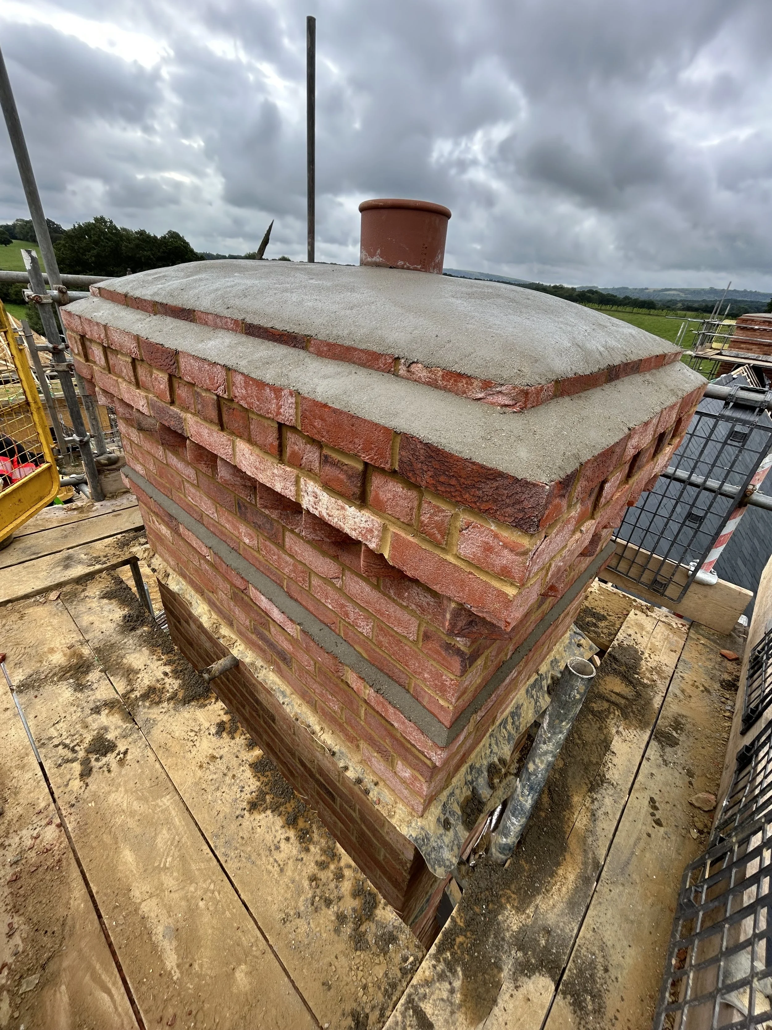 Close-up of a brick chimney under construction on a rooftop with cloudy sky overhead.