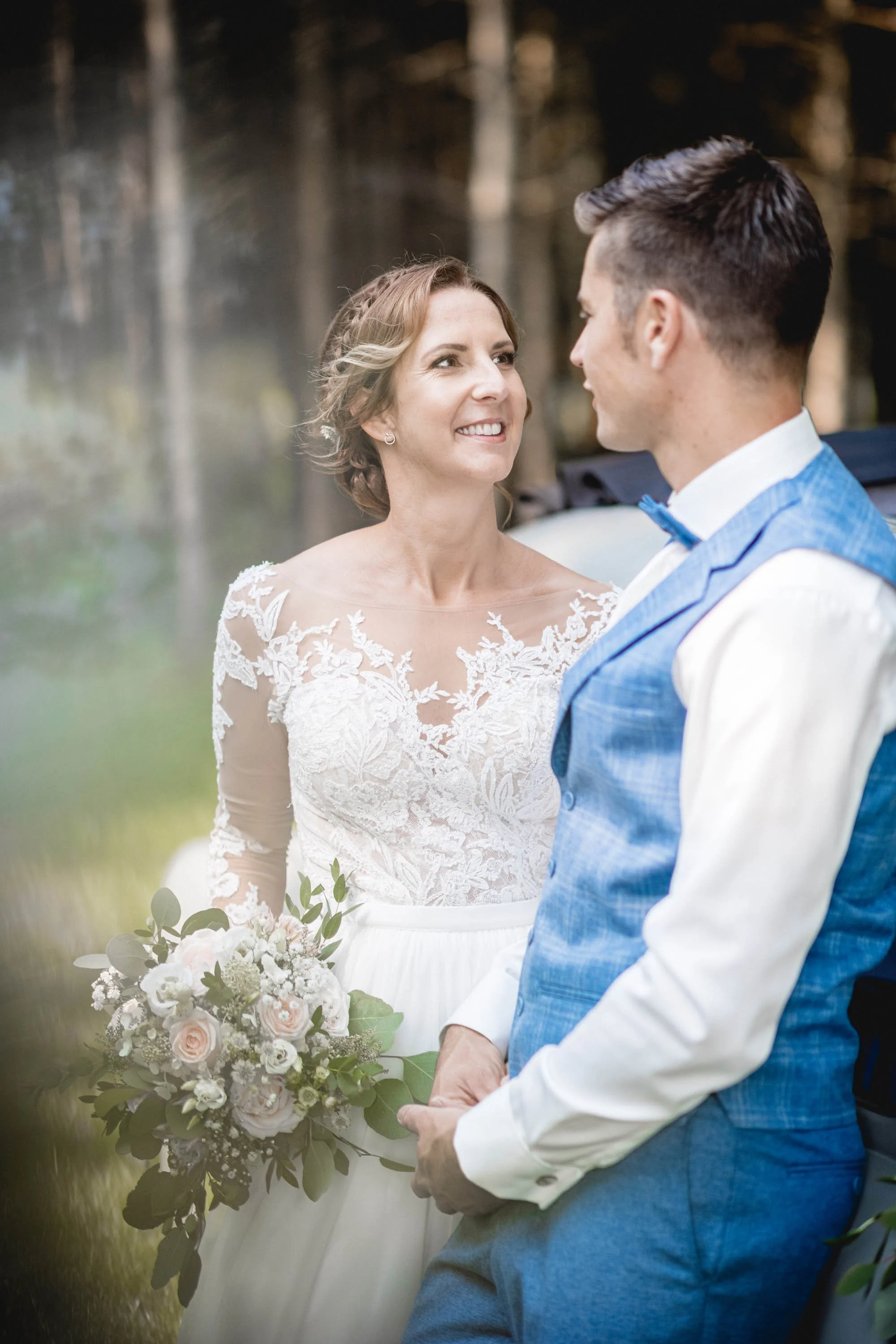 Braut und Bräutigam stehen sich bei ihrer Hochzeit im Grünen gegenüber, die Braut hält einen Blumenstrauß.