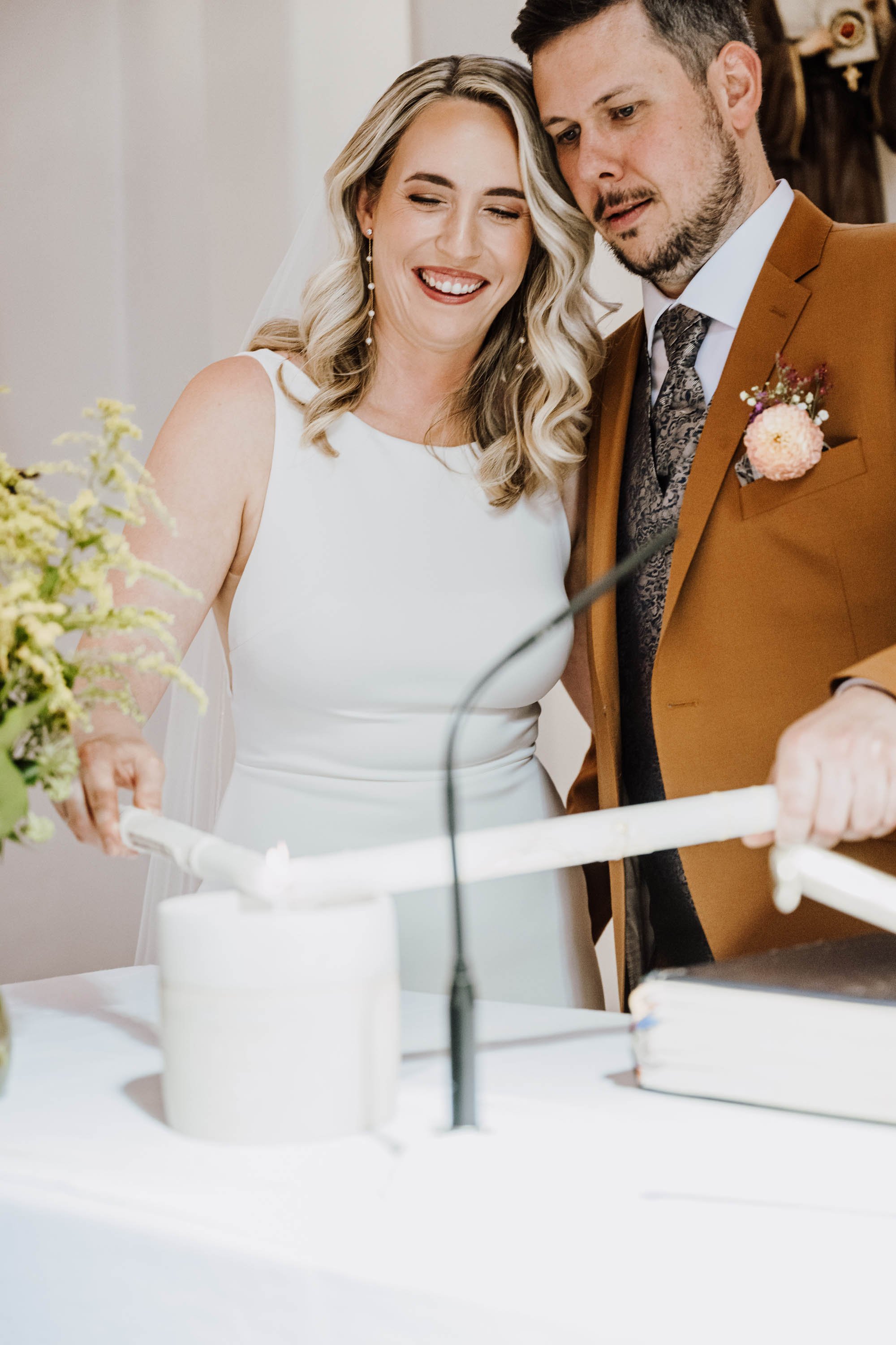 Ein brauner Kleid und ein Anzug trugene Hochzeitspaar schneidet gemeinsam eine Hochzeitstorte.