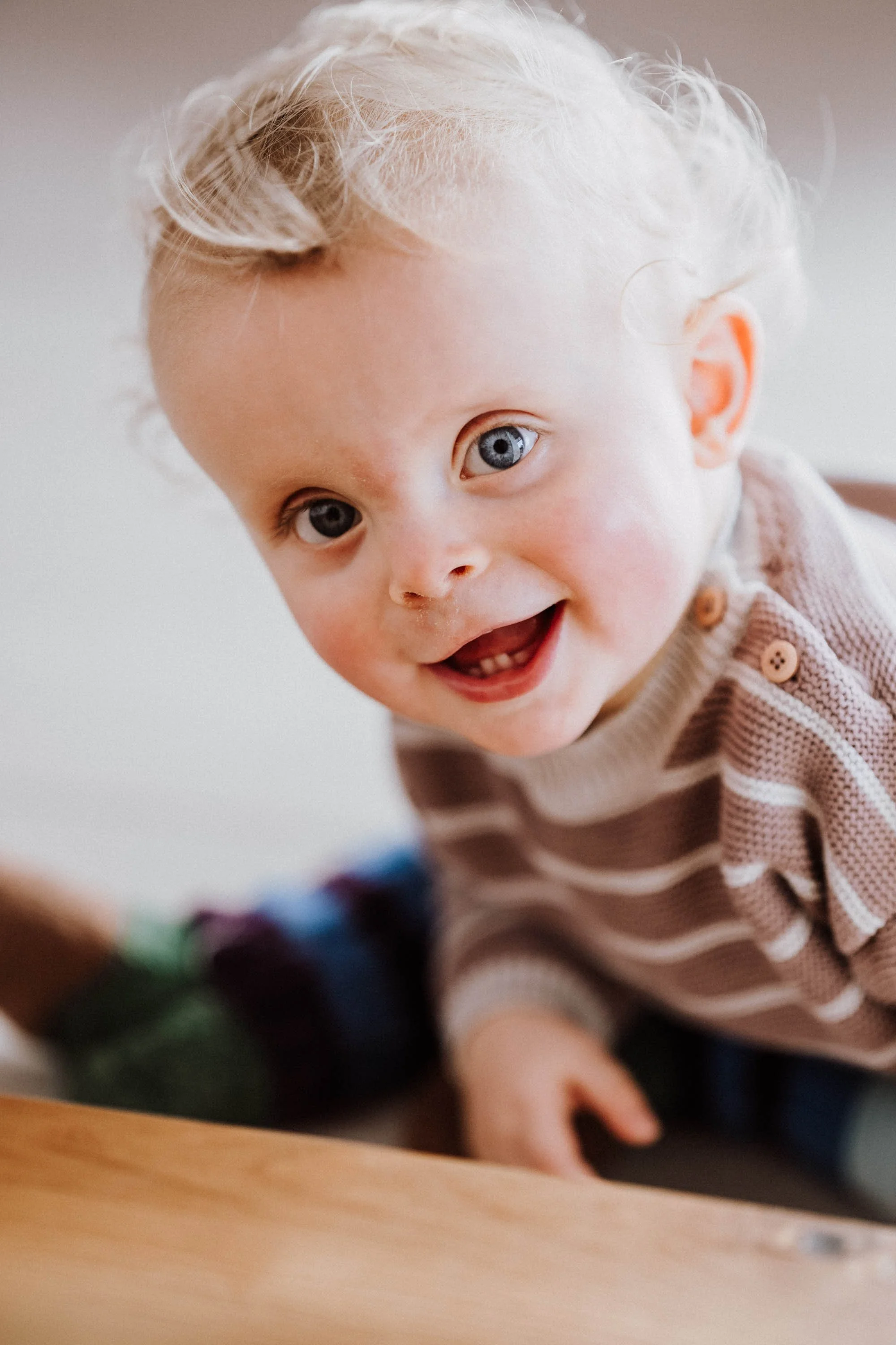Lächelnder kleiner Junge mit blonden Haaren und blauen Augen, trägt ein braun-weiß gestreiftes Hemd in Nahaufnahme.