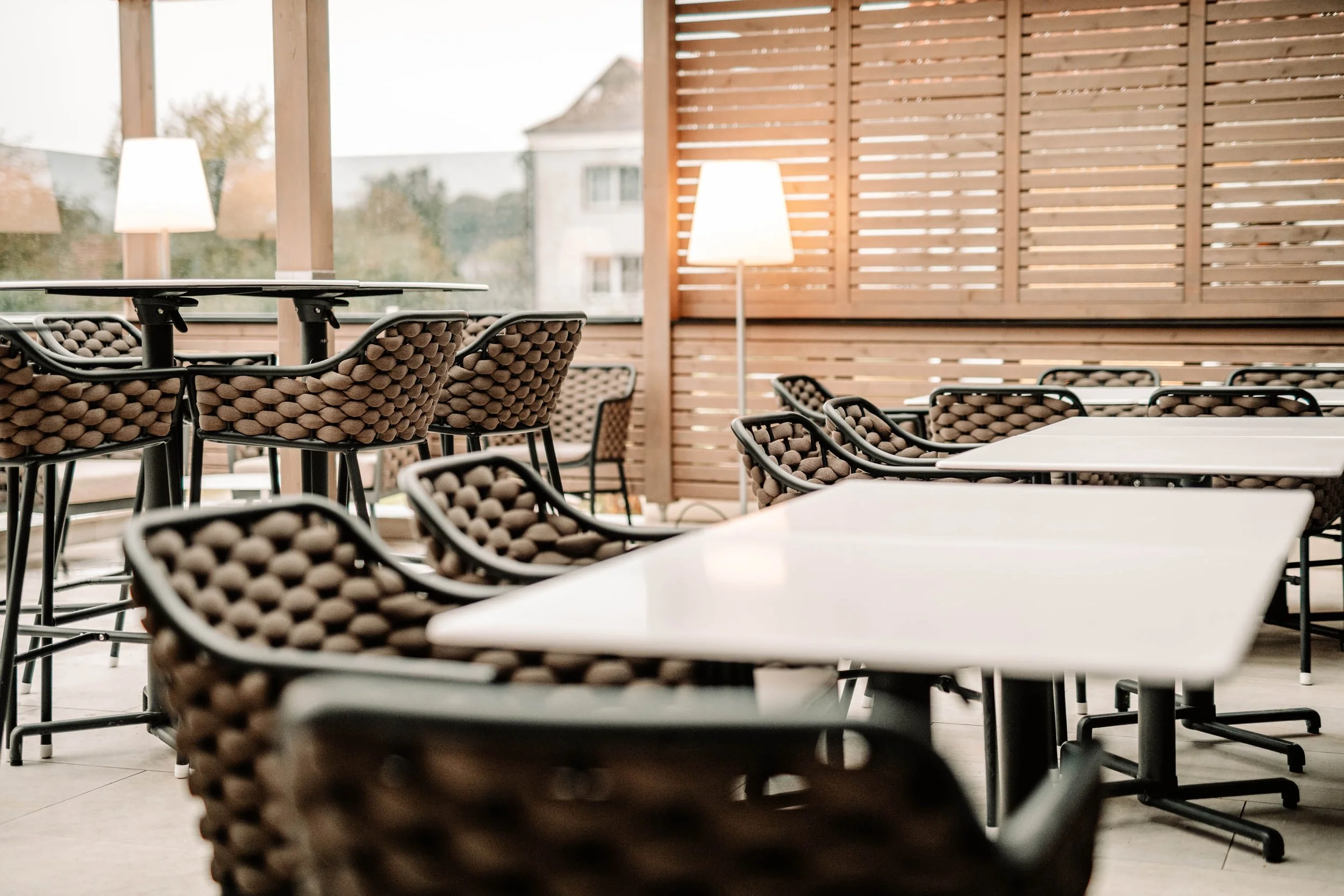 Leere Sitzgelegenheiten mit weißen Tischen in einem modern gestalteten Raum mit Holzverkleidung und Stehlampen.