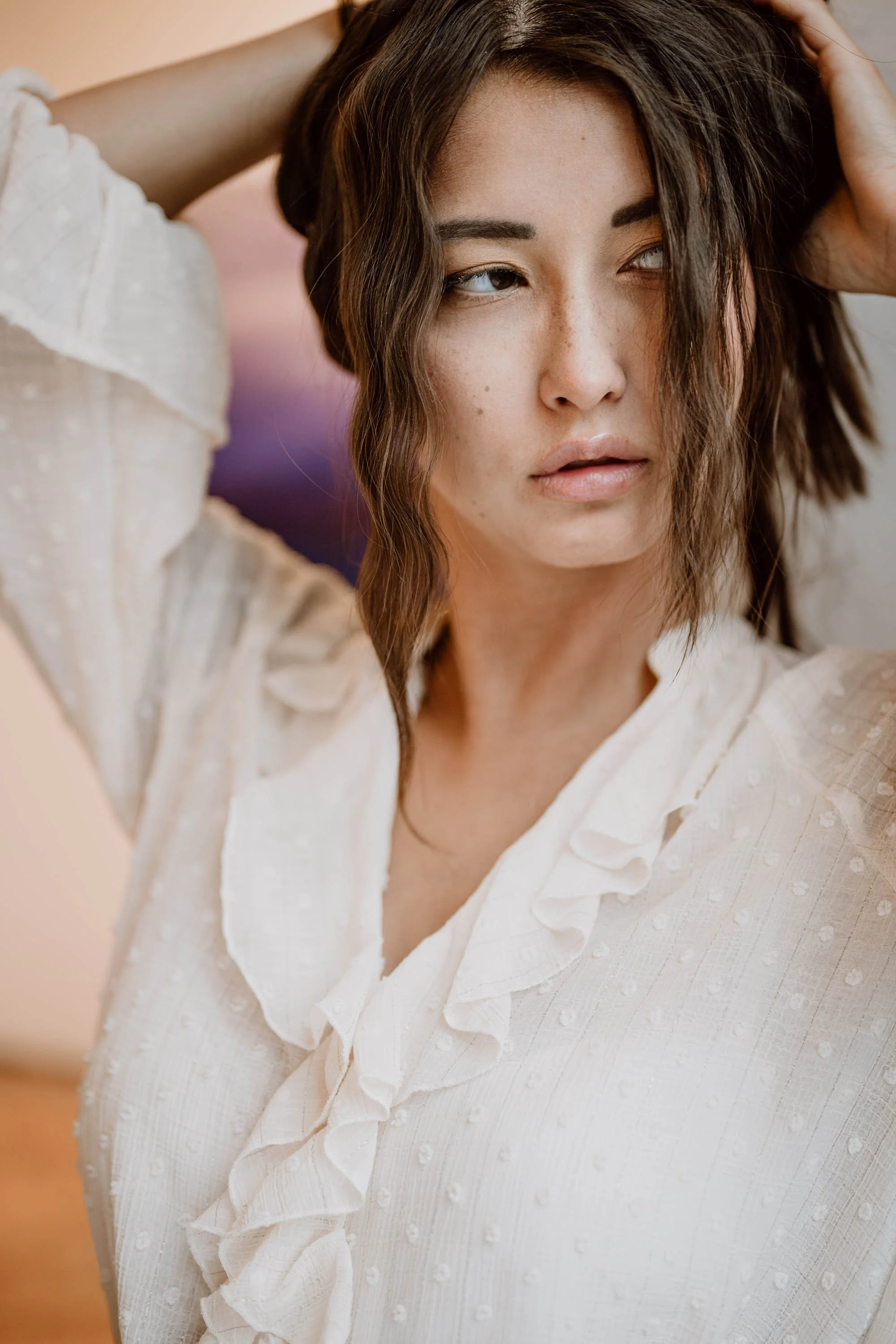 Nahaufnahme einer Frau mit schulterlangem, leicht gewellten braunen Haar, die einen weißen Bluse mit Rüschen trägt und nach links schaut.