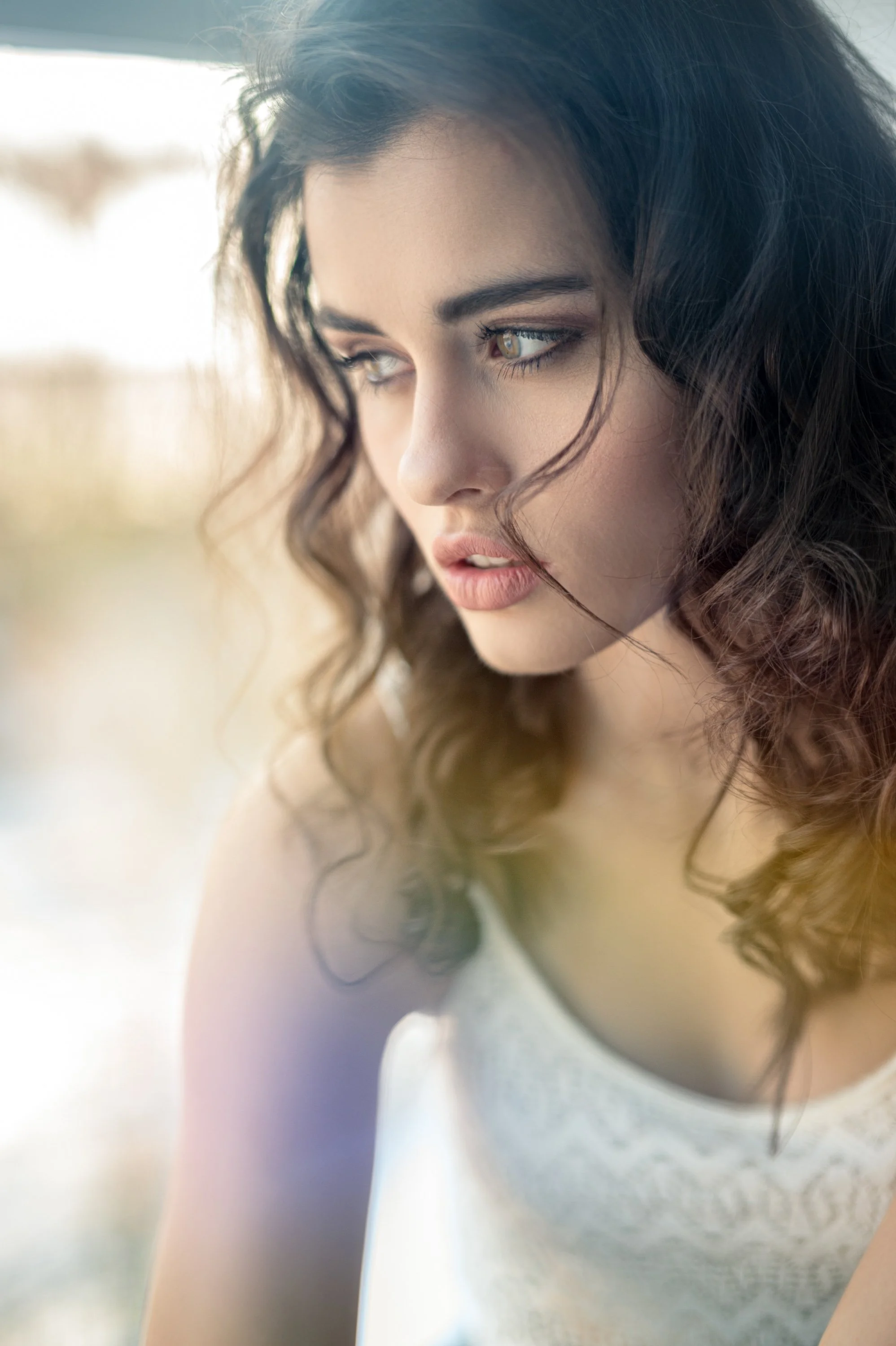 Nahaufnahme eines jungen Mädchens mit lockigem braunem Haar und nachdenklichem Gesichtsausdruck, im Freien bei Sonnenlicht fotografiert.