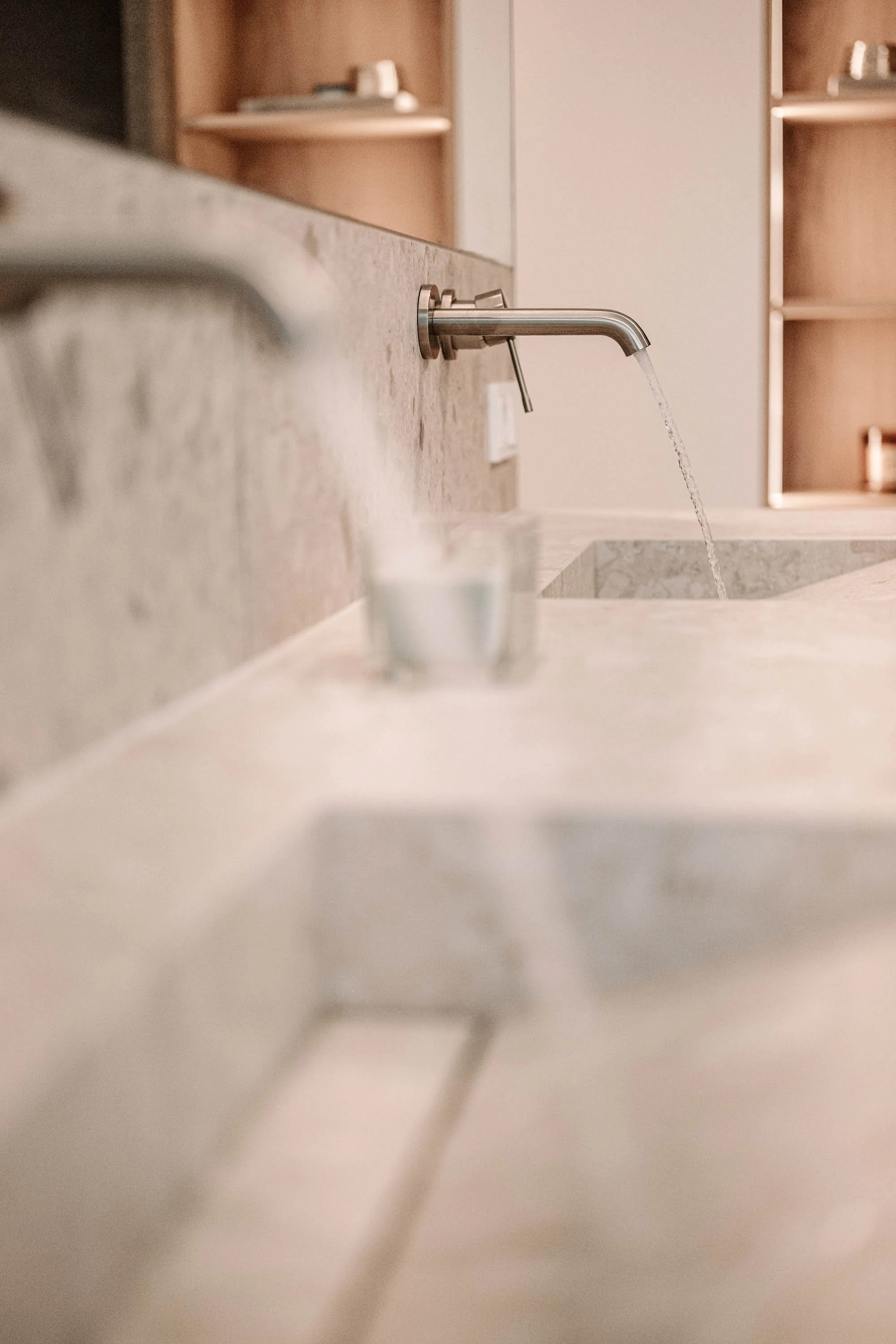 Ein Wasserhahn, aus dem Wasser in eine Spüle fließt, mit unscharfen Gegenständen im Vordergrund.