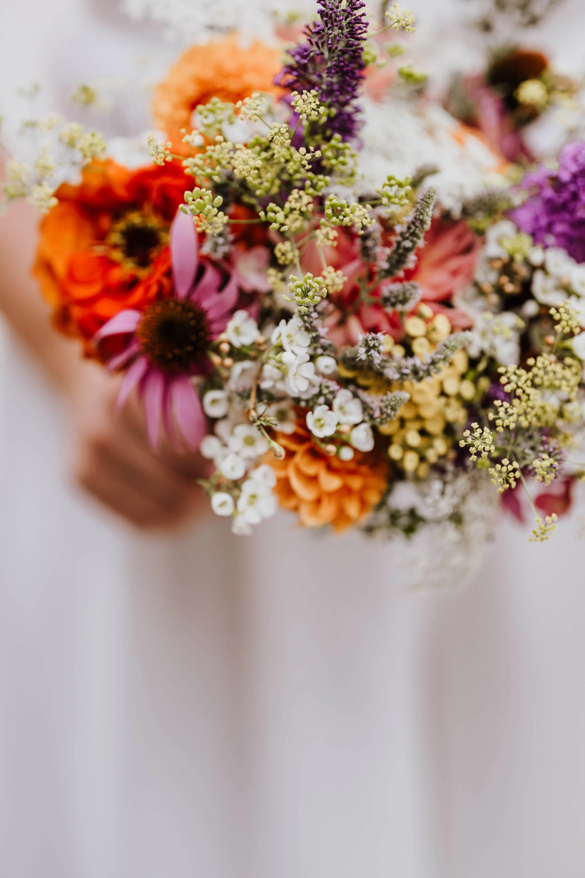 Bunter Blumenstrauß mit verschiedenen Blumen in Gelb, Orange, Lila, Rosa und Weiß, gehalten in einer Hand