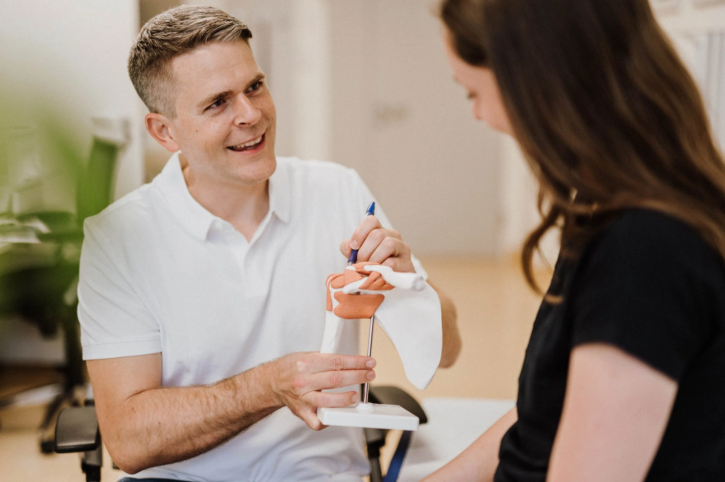 Ein Mann erklärt einer Frau einen anatomischen Schulungsmodellarm, vermutlich in einer medizinischen Beratung oder Schulung.