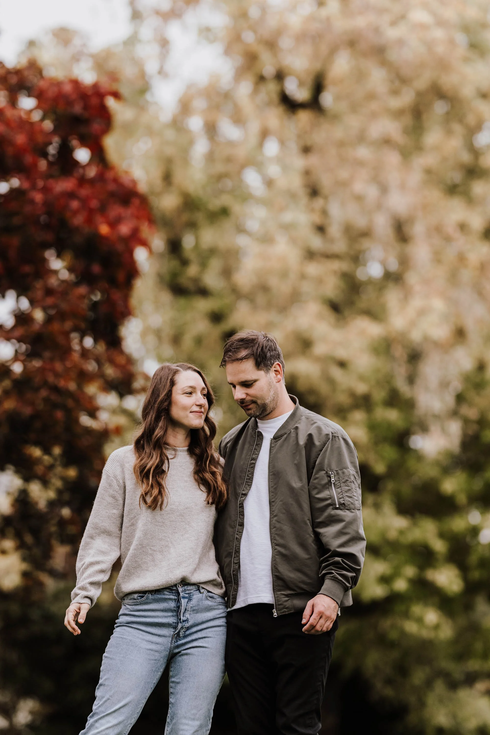 Ein Paar, ein Mann und eine Frau, stehen eng zusammen im Park mit herbstlicher Laubfärbung und schauen sich zärtlich an.