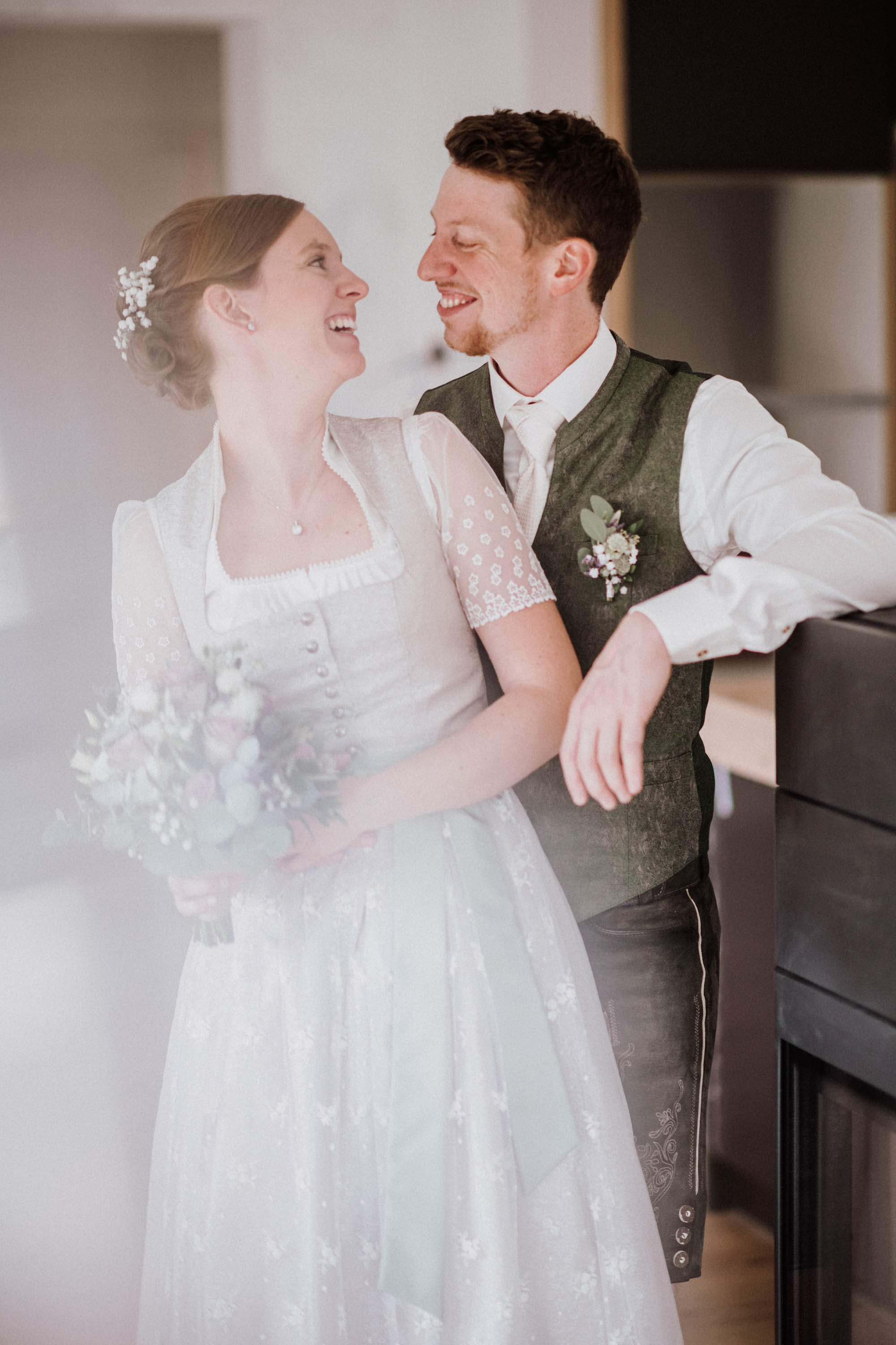 Ein glückliches Brautpaar auf ihrer Hochzeit, die Frau trägt ein traditionelles Kleid mit Blumen im Haar, der Mann trägt eine Trachtenweste mit Krawatte.