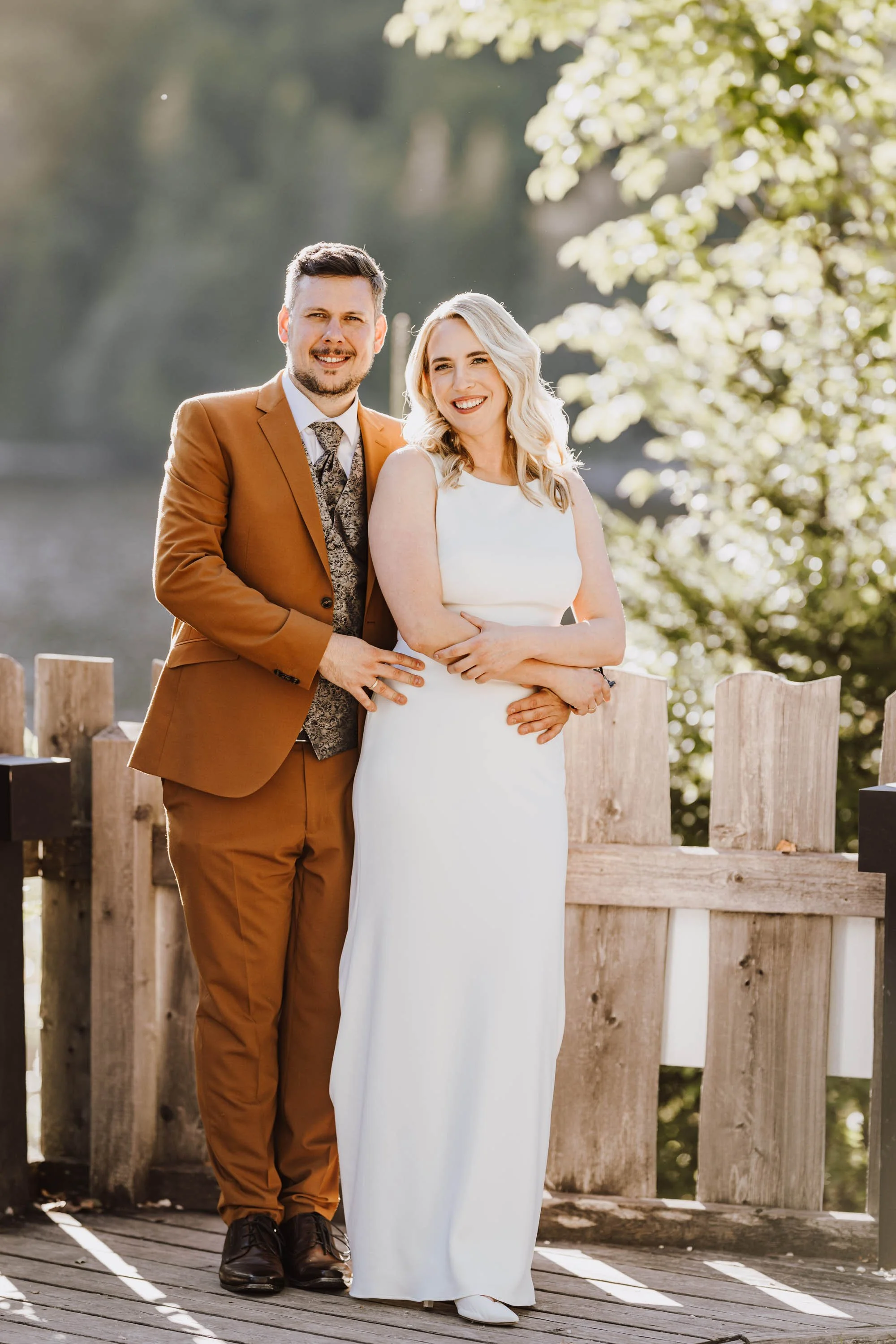 Ein glücklich verheiratetes Paar steht auf einer Holzbrücke bei Sonnenuntergang, umgeben von Natur, beim Ja-Wort