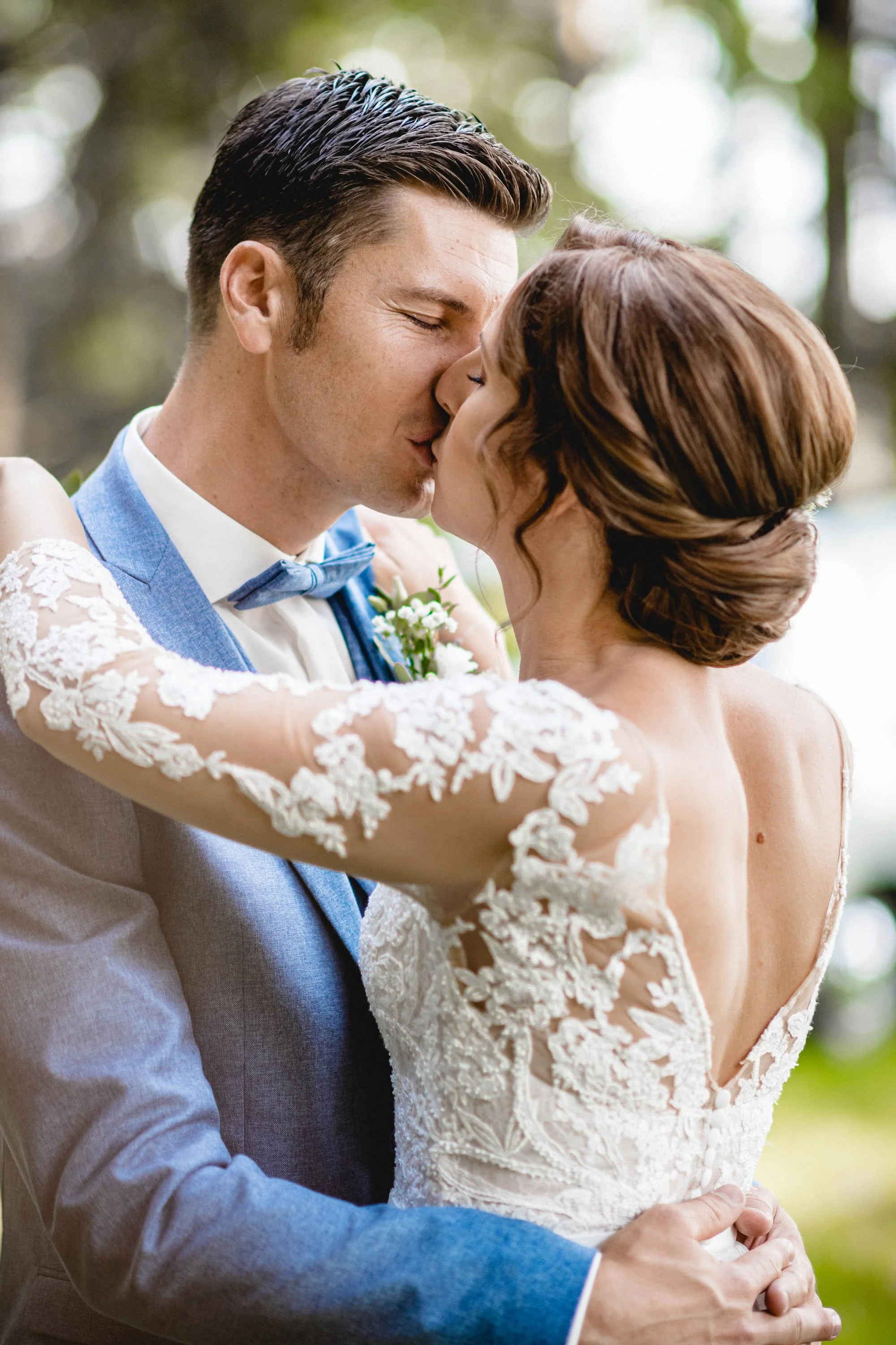 Ein Brautpaar küsst sich bei einer Hochzeit im Freien, die Frau trägt ein Spitzenkleid und der Mann einen Anzug mit Fliege.