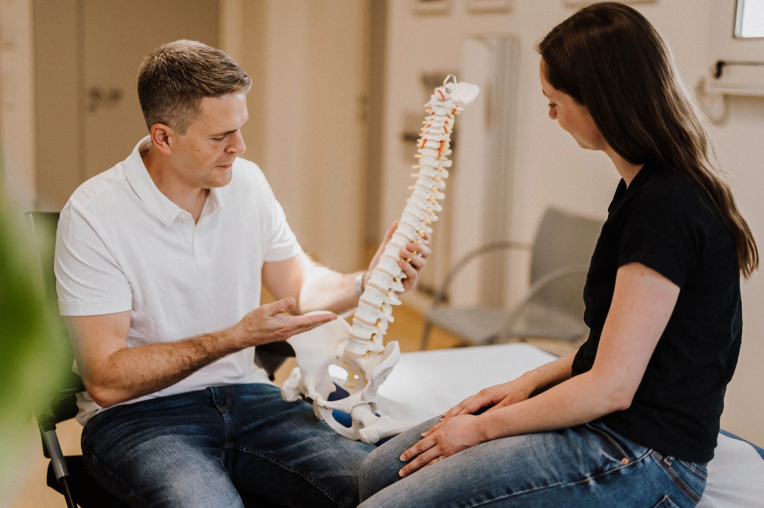 Ein Arzt erklärt einer jungen Frau die Wirbelsäule anhand eines modellierten Skeletts.