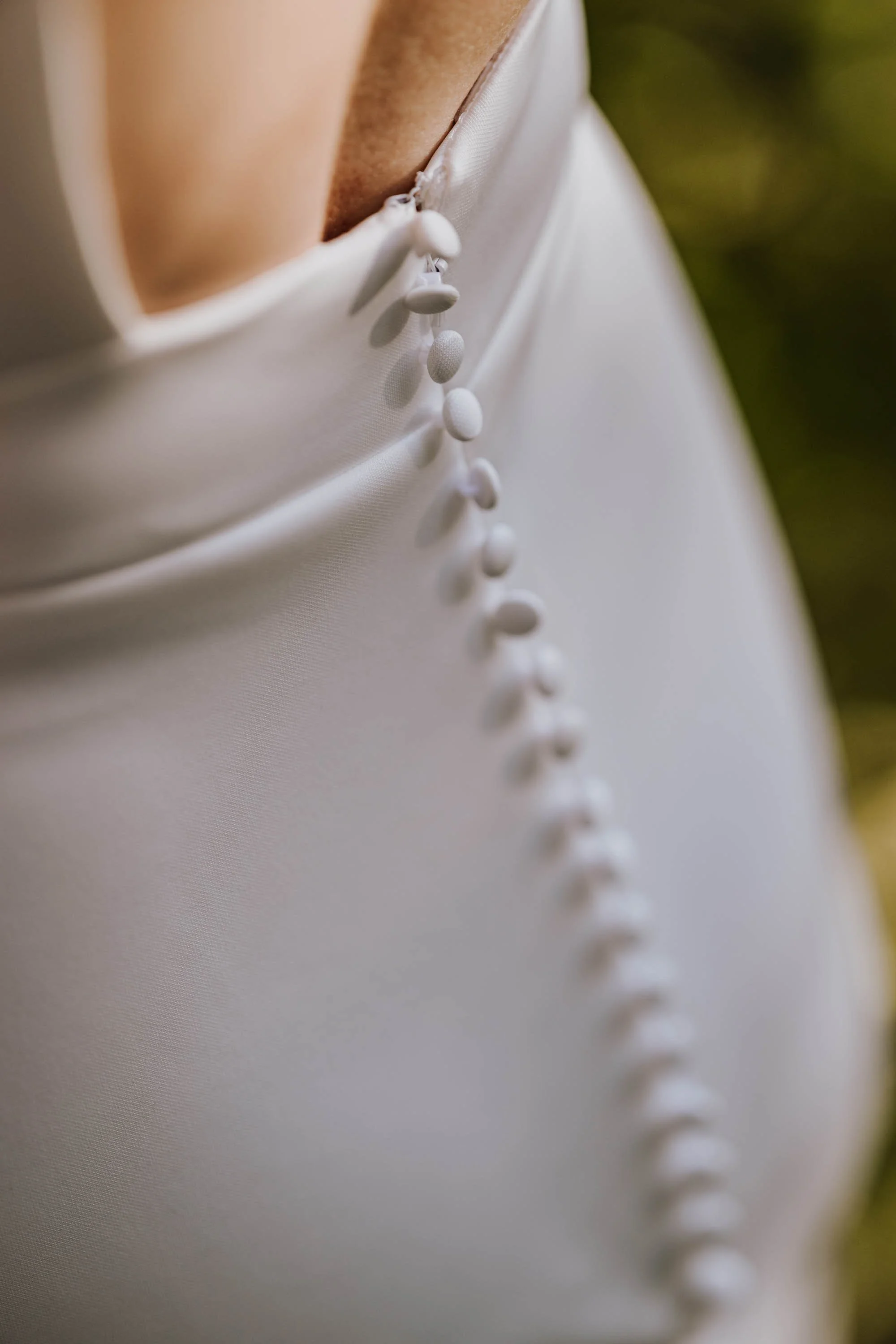Nahaufnahme eines weißen Kleides mit Knöpfen auf der Rückseite, vermutlich ein Brautkleid.