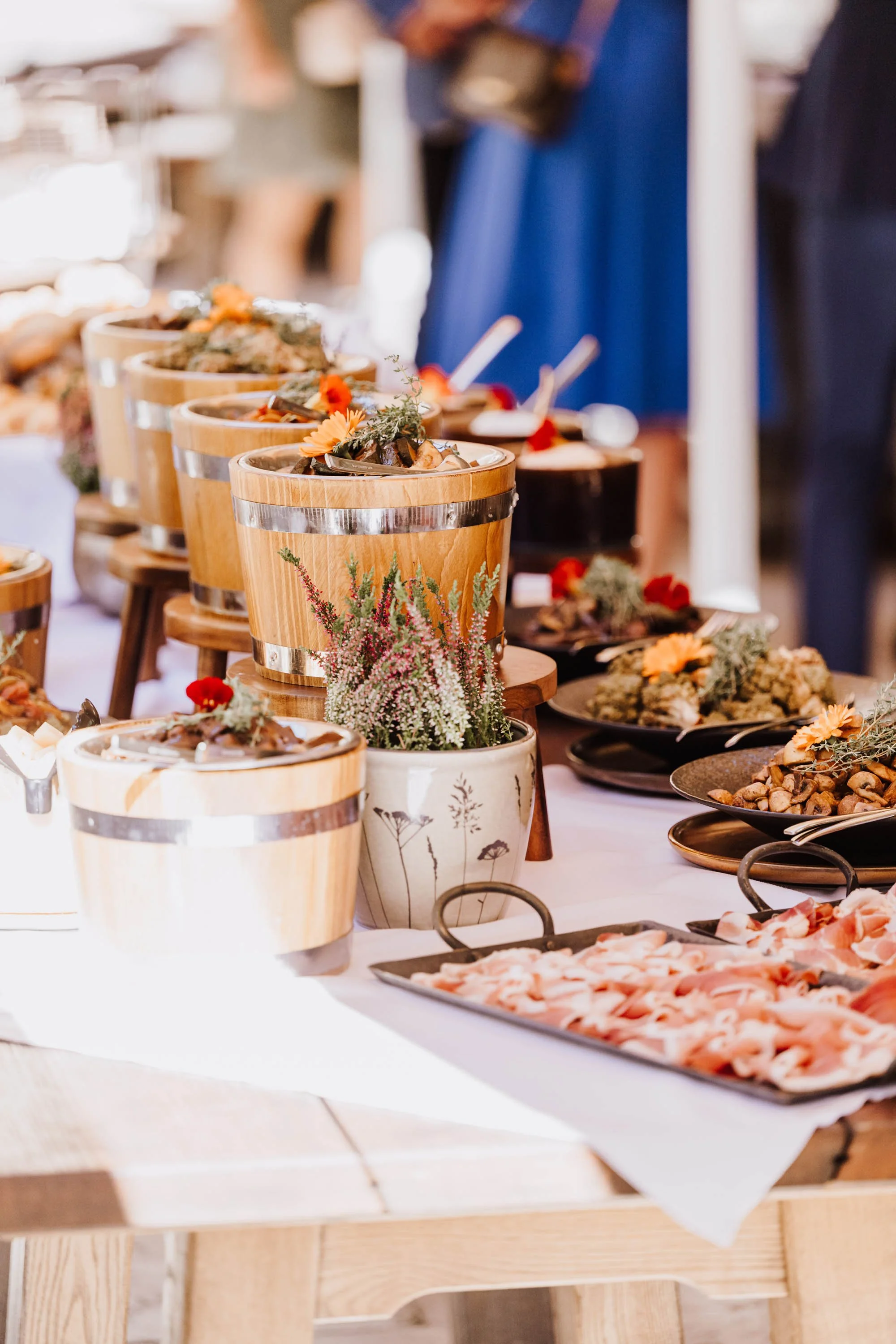 Verschiedene Antipasti, darunter gepresster Schinken, auf einem Buffet mit weißen Tischdecken, dekoriert mit Blumen in Töpfen und Holzschüsseln.