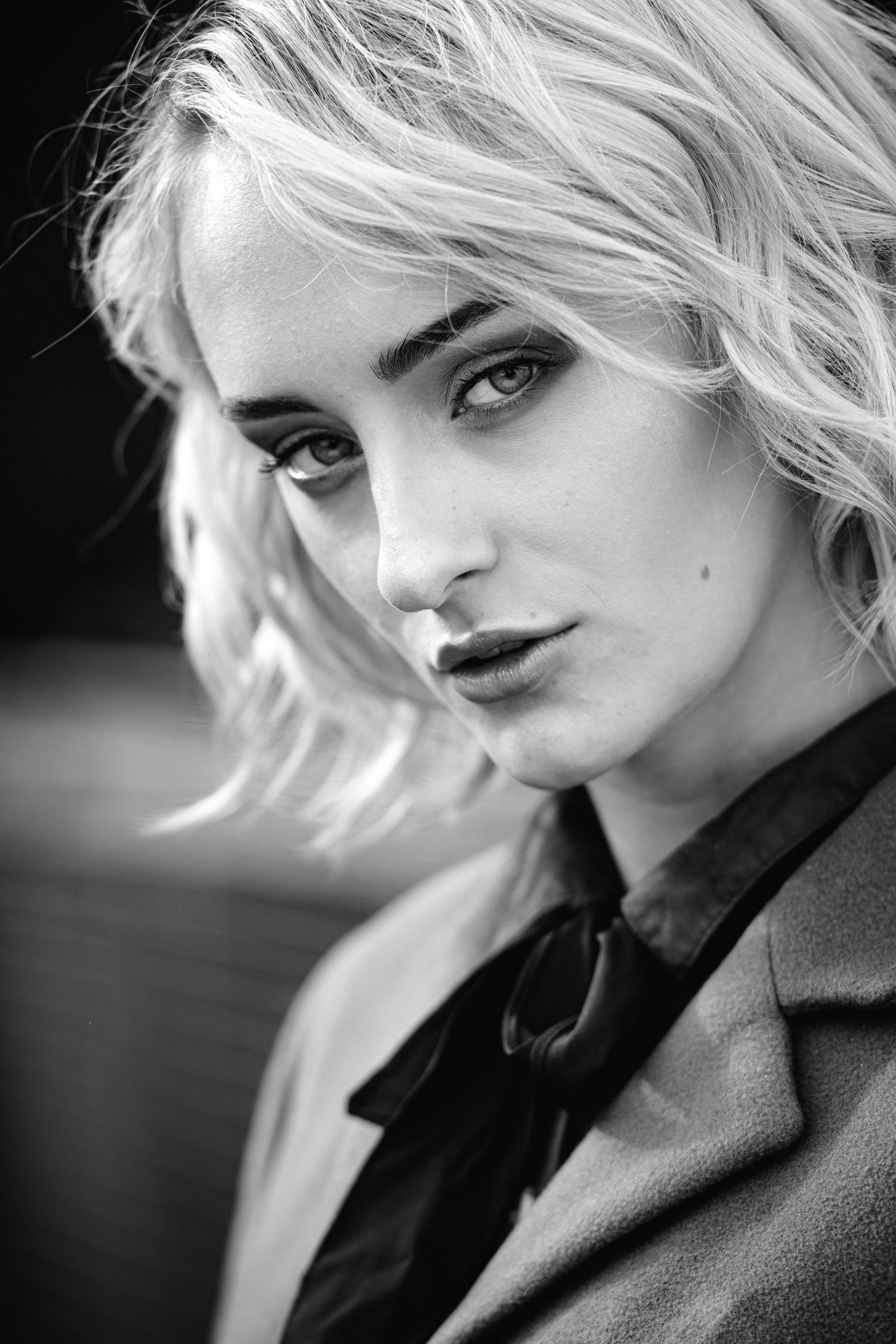 Schwarz-Weiß-Porträt einer jungen Frau mit kurzen, lockigen Haaren, die einen dunklen Lippenstift trägt und eine dunkle Schleife an ihrer Kleidung hat.