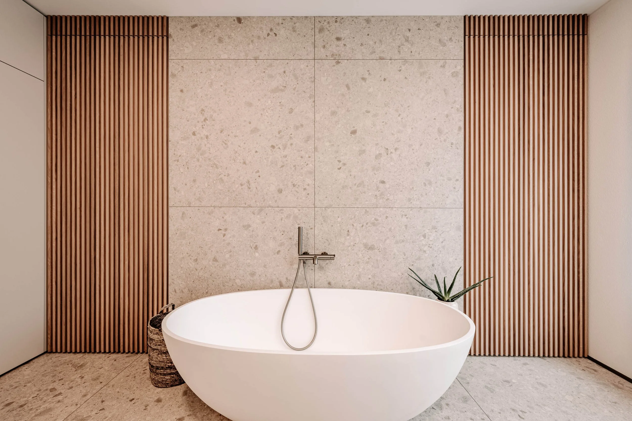 Moderner Badezimmerspiegel mit Badewanne, Holzwandverkleidung und Pflanze im Hintergrund.