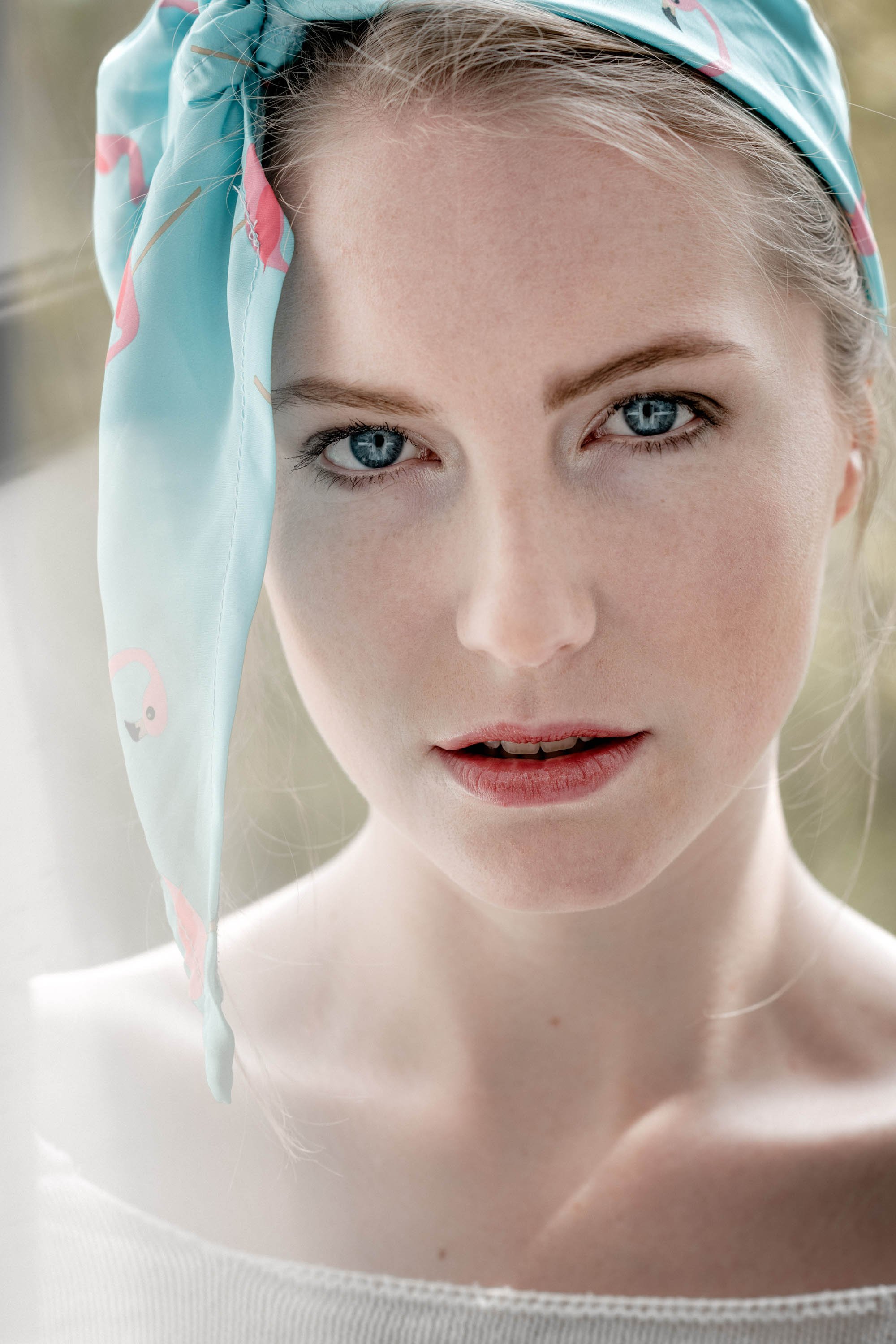 Nahaufnahme eines jungen Mädchens mit blauen Augen, das einen hellblauen Tuch mit Flamingo-Motiv trägt.