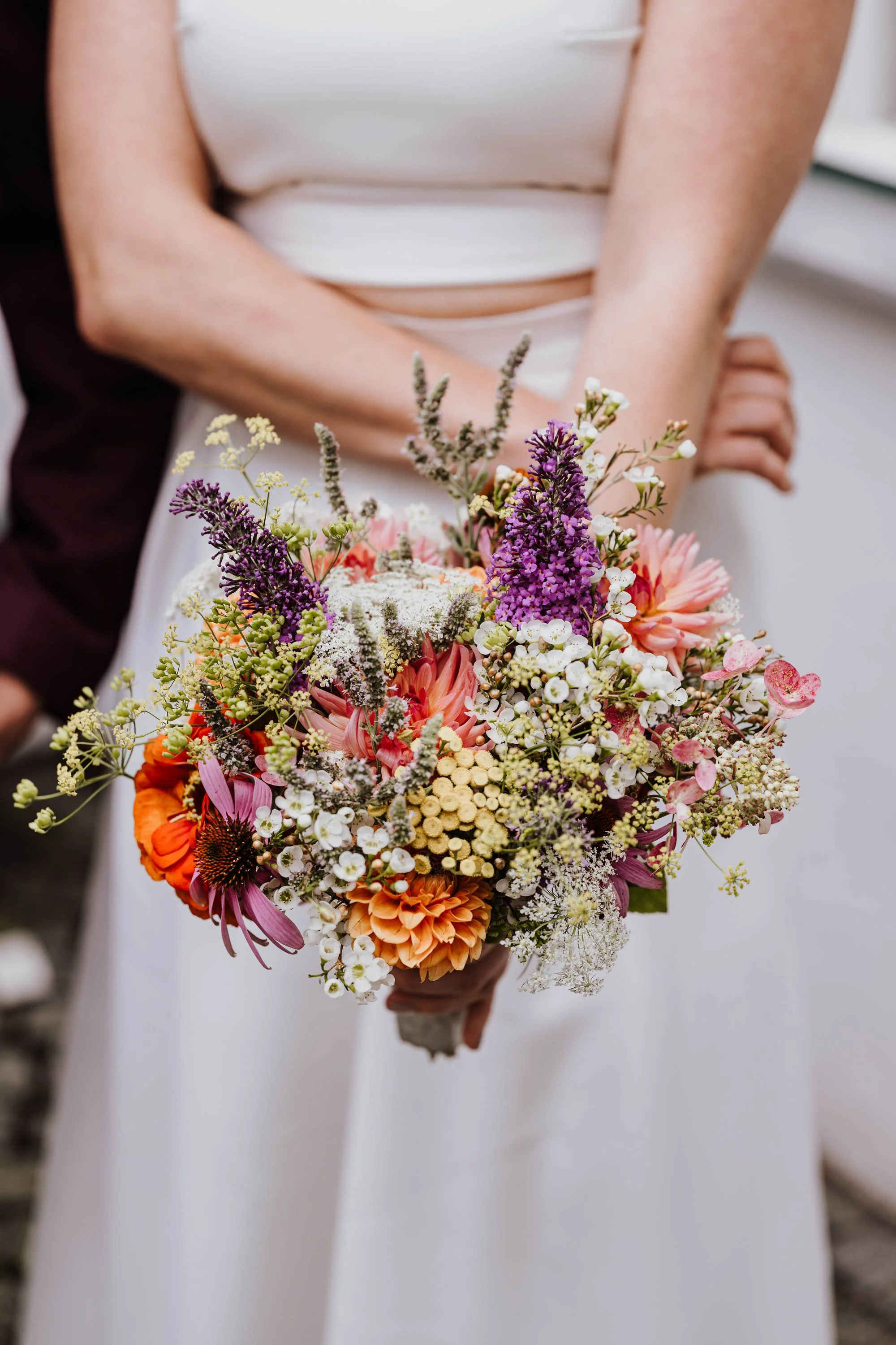 Braut hält einen bunten Blumenstrauß mit verschiedenen Blumen in Pink, Lila, Weiß und Orange beim Hochzeitstag.