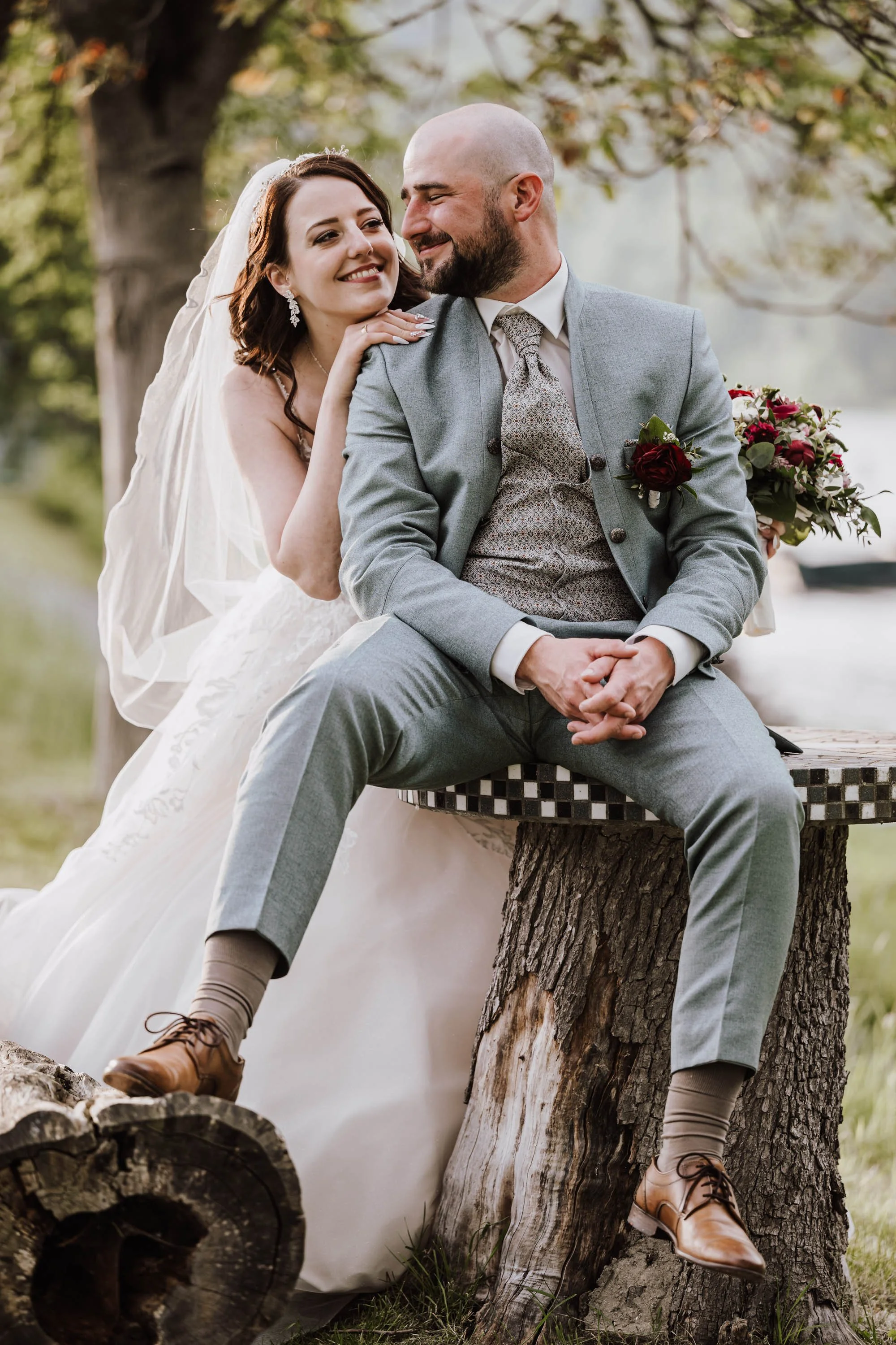 Ein Paar bei einer Hochzeit im Freien, lachend und umarmend, mit Blumen im Hintergrund.