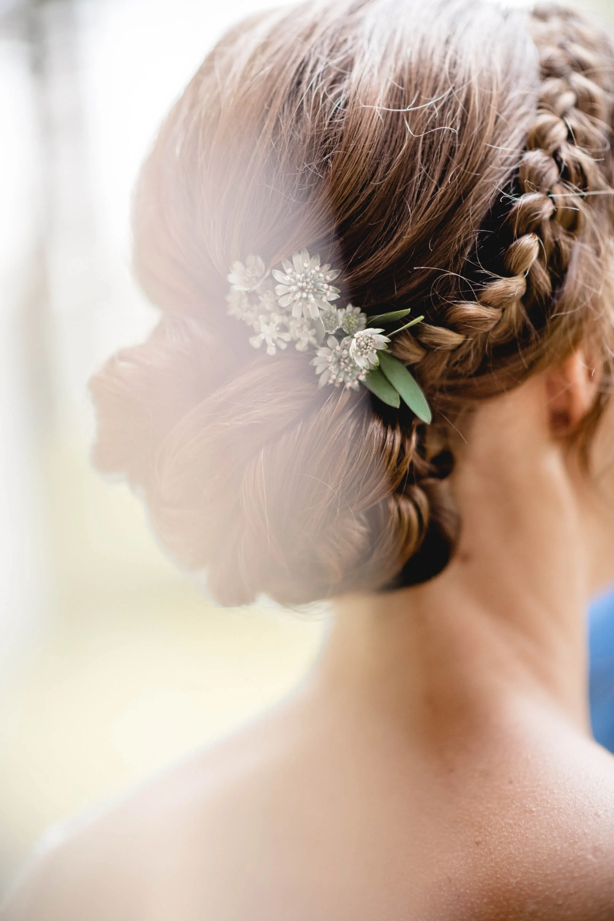 Nahaufnahme eines Damenhaarschnitts mit schwer geflochtenem Haar und weißen Blumen als Haarschmuck.