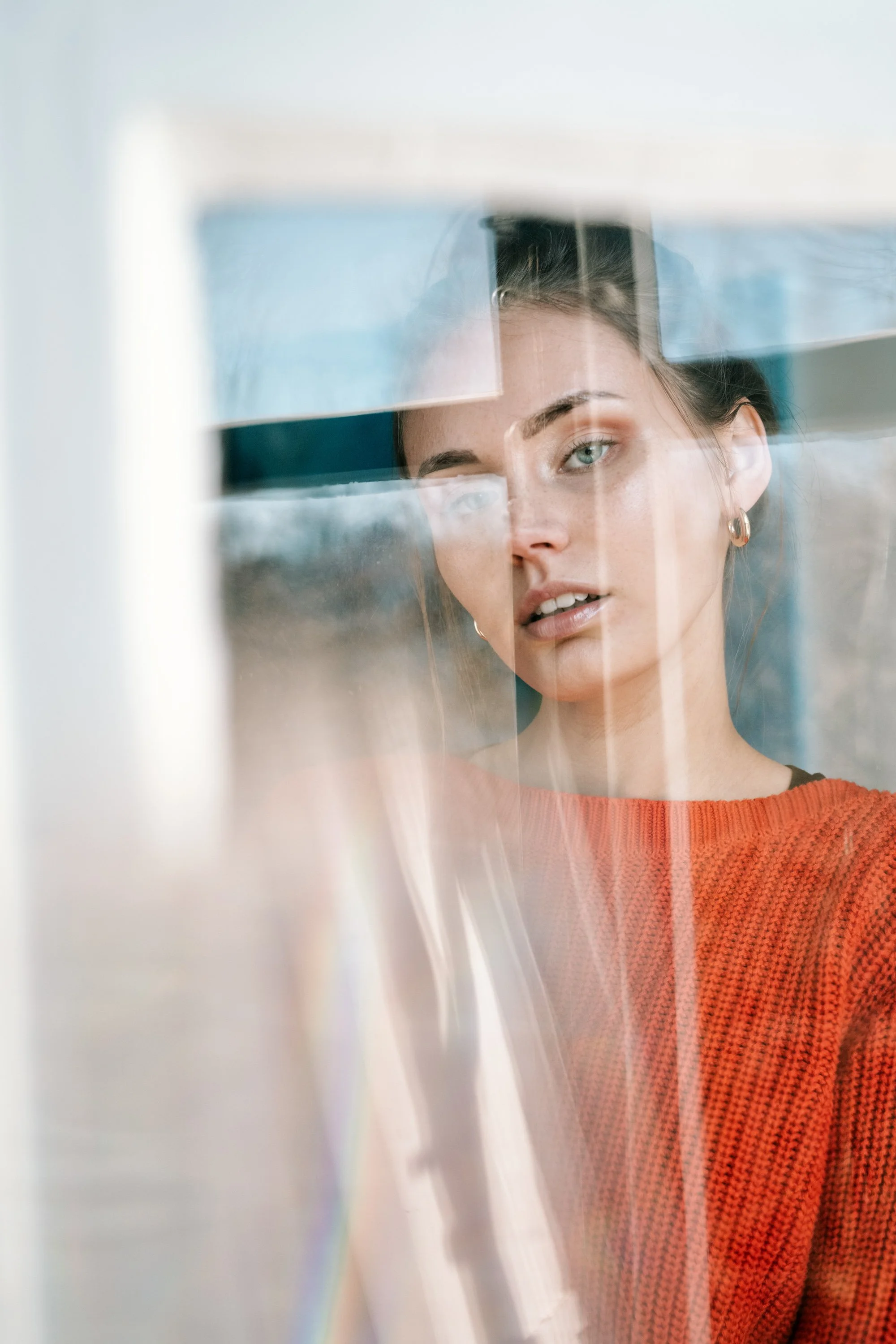 Ein junges Mädchen mit blauen Augen und braunen Haaren, das durch eine Glasscheibe schaut.