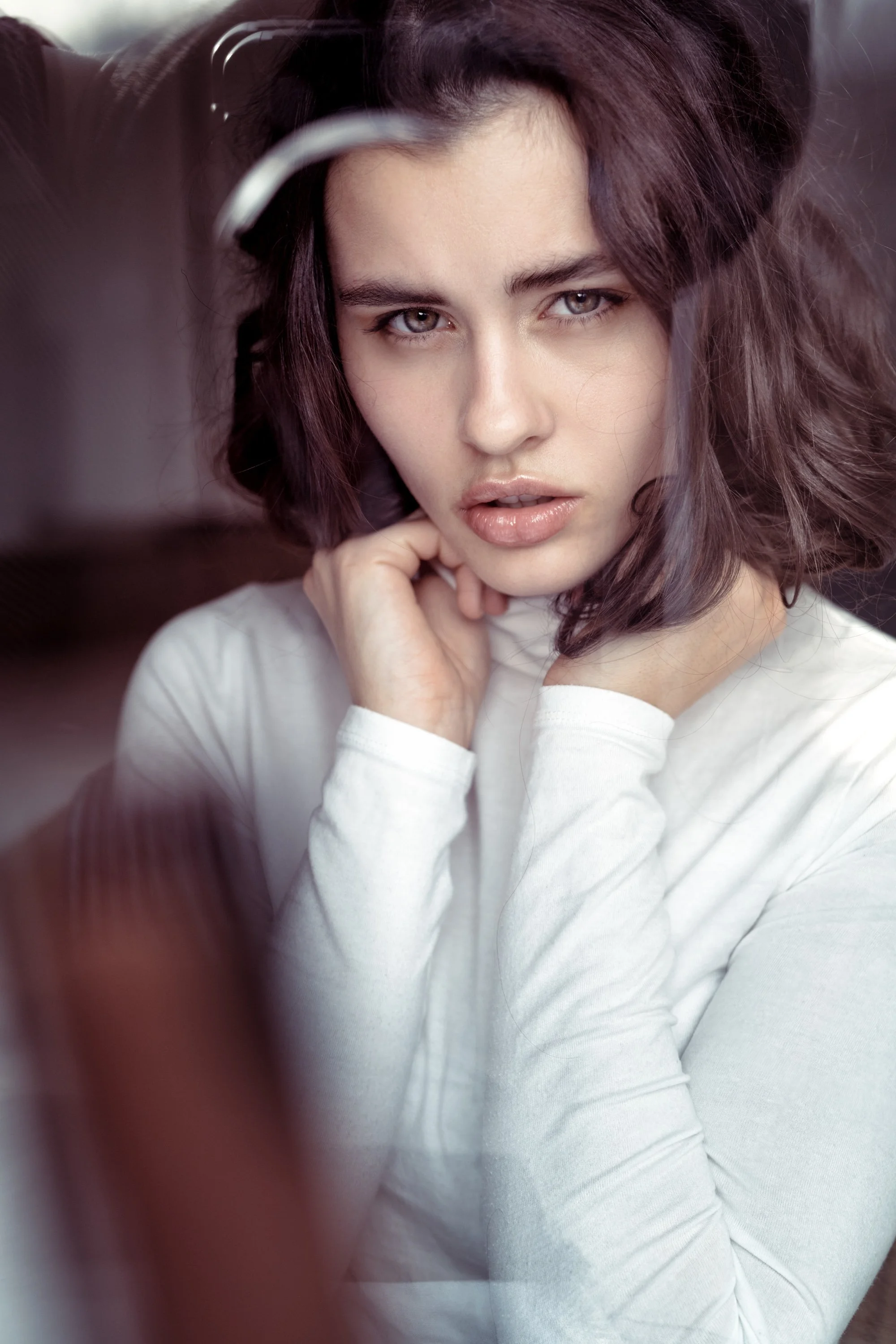 Nahaufnahme einer jungen Frau mit braunen, gewellten Haaren, die in die Kamera blickt und ihre Hand an die Wange legt.